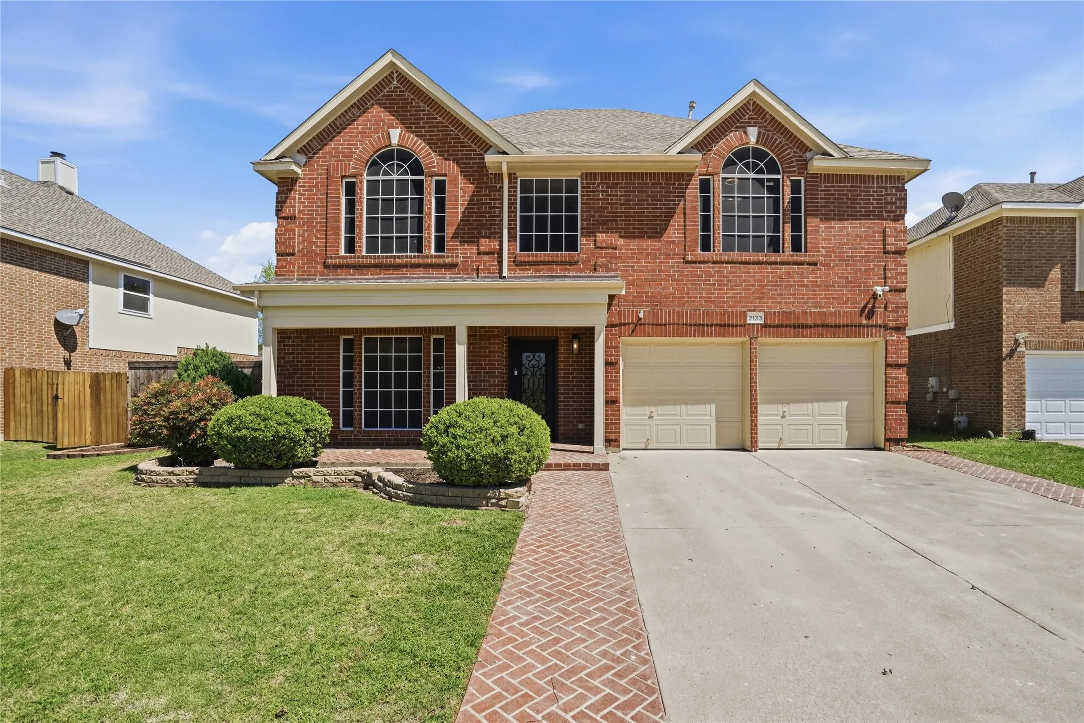 Traditional-style home with brick siding, an attached garage, driveway, covered porch, and roof with shingles