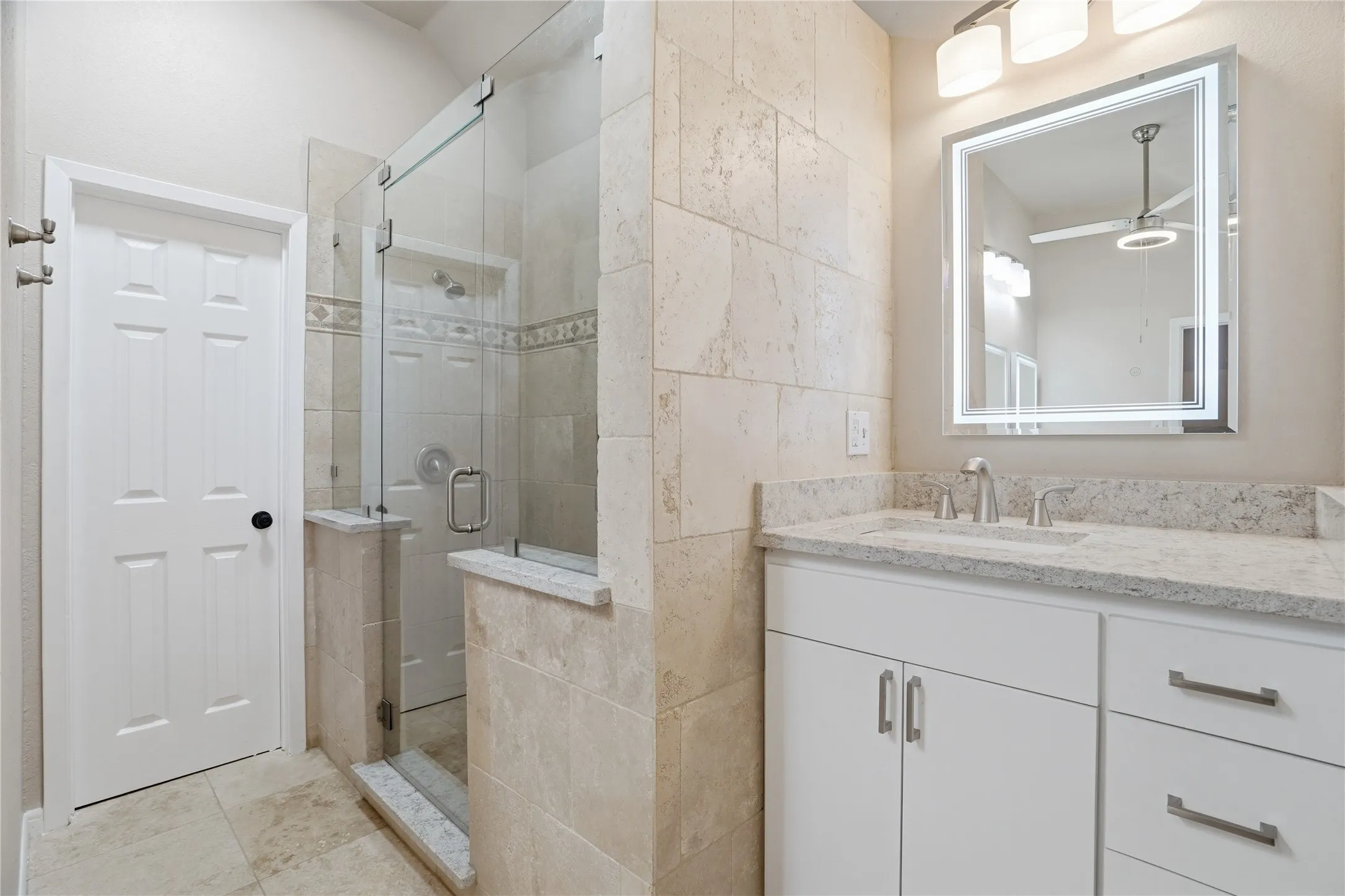 Primary bathroom featuring vanity, a stall shower, a ceiling fan, and light tile patterned floors