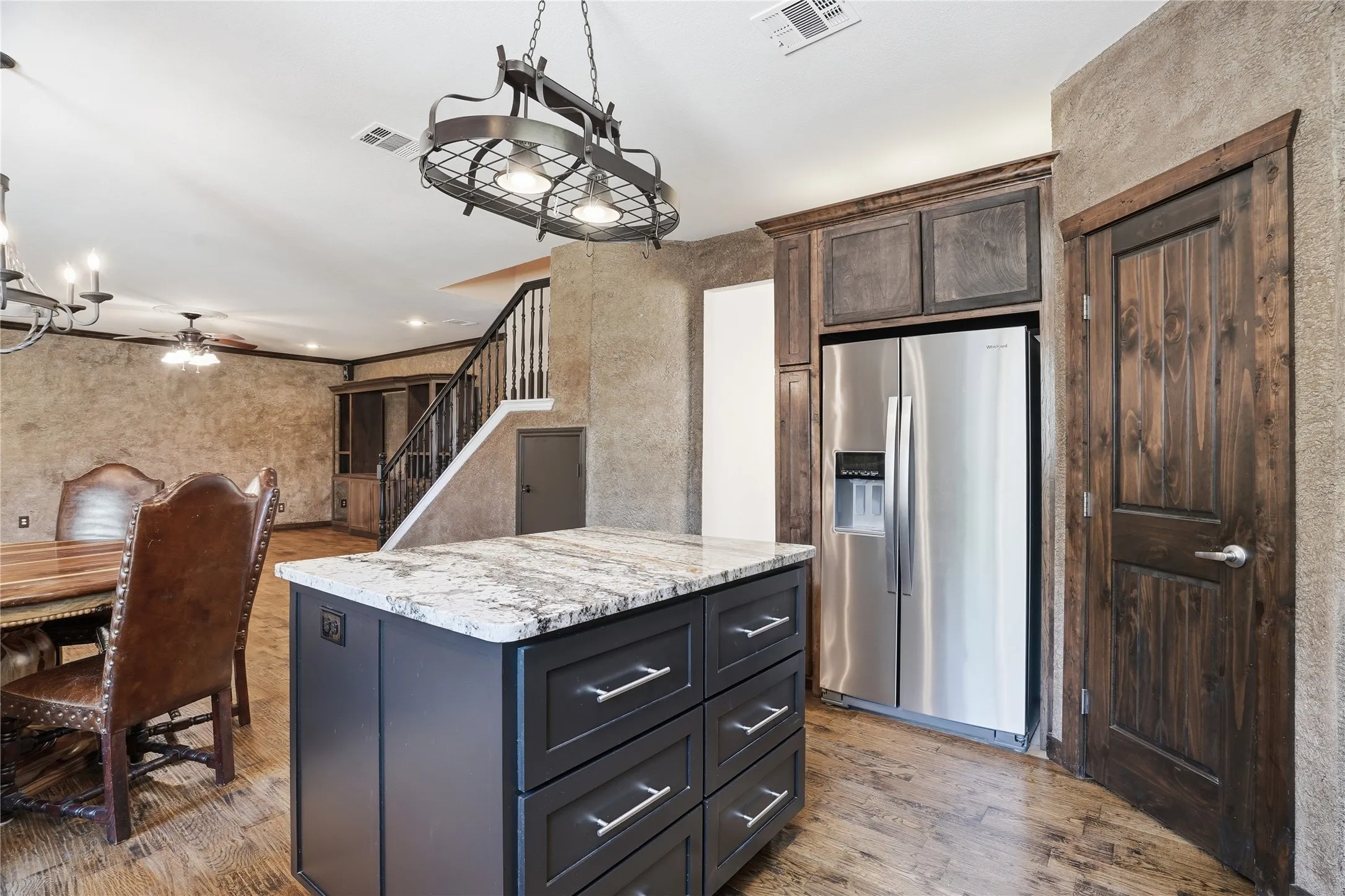 Kitchen featuring stainless steel refrigerator with ice dispenser, a kitchen island, light wood finished floors, light stone countertops, and hanging lights