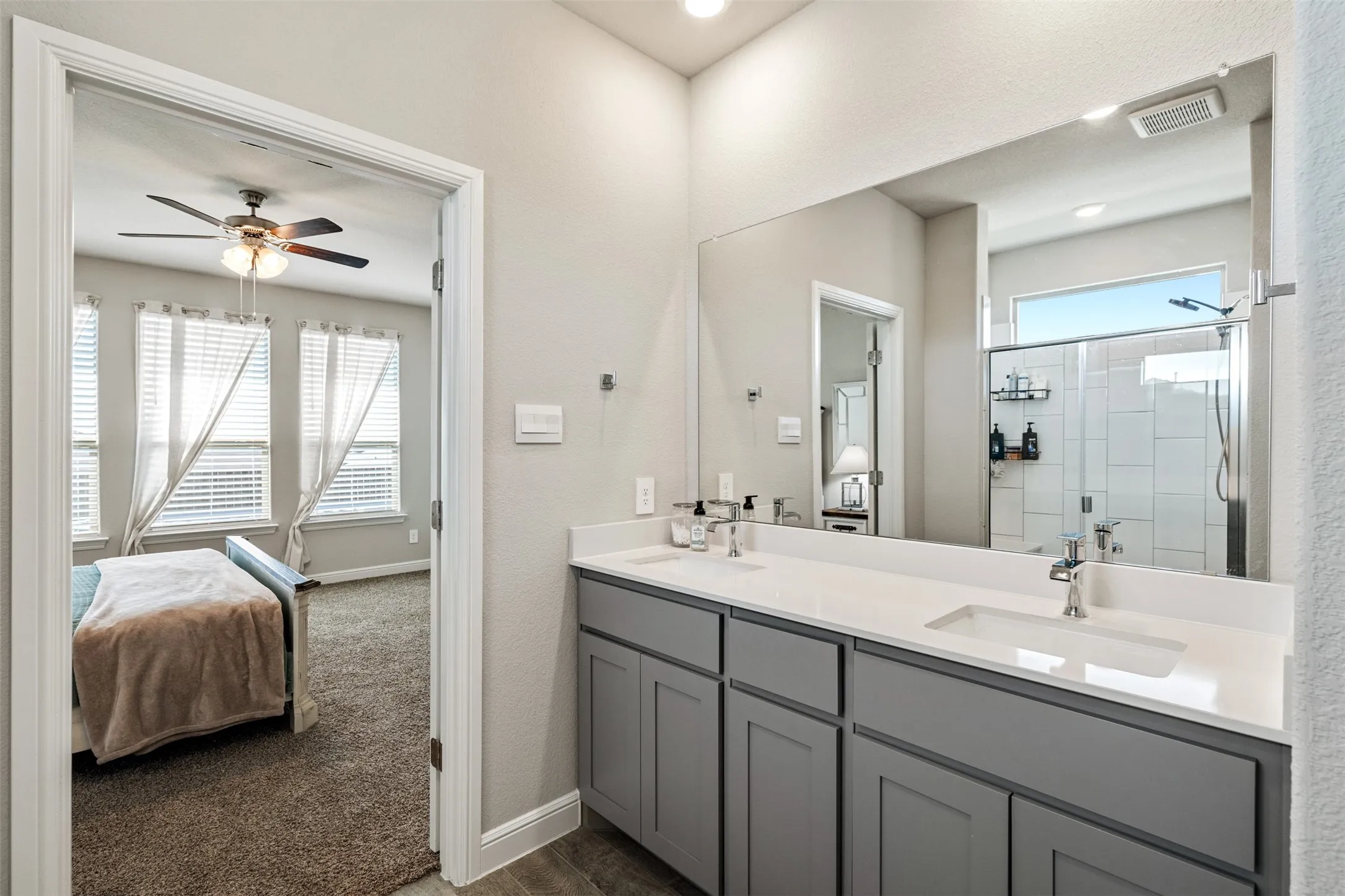 Ensuite bathroom featuring double vanity, a shower stall, a ceiling fan, dark wood finished floors, and dark colored carpet