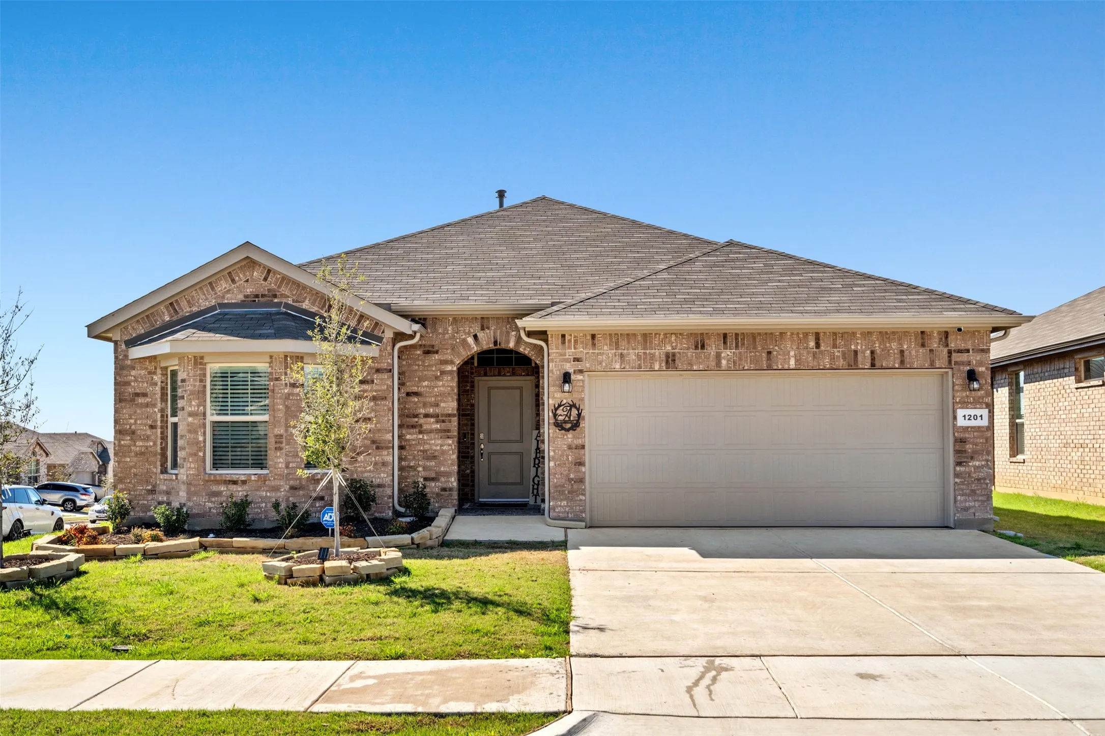 View of front of house featuring a garage, driveway, brick siding, a front yard, and roof with shingles