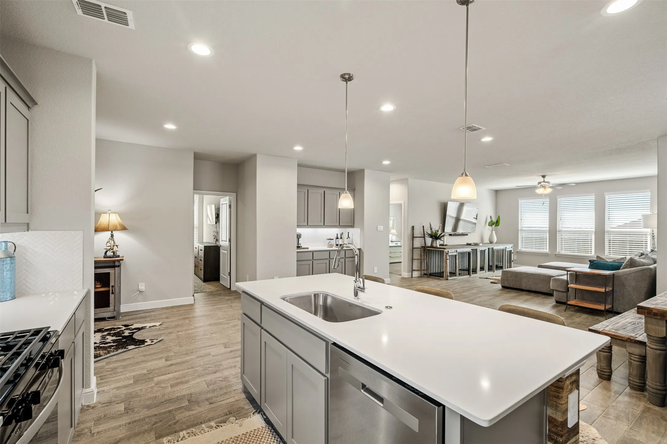 Kitchen with gray cabinets, open floor plan, stainless steel appliances, a center island with sink, and light wood finished floors