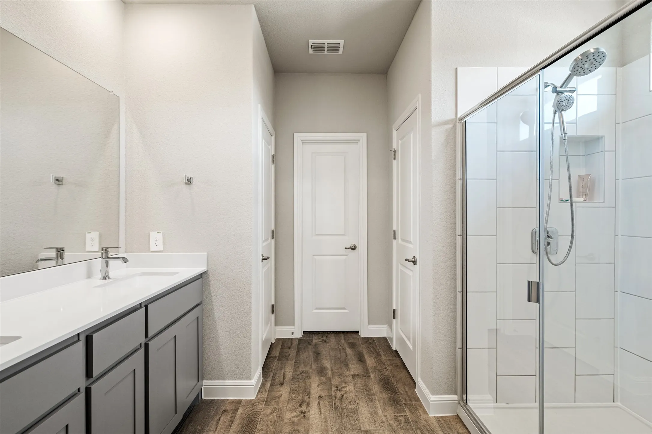 Full bathroom featuring double vanity, a shower stall, and dark wood-style floors