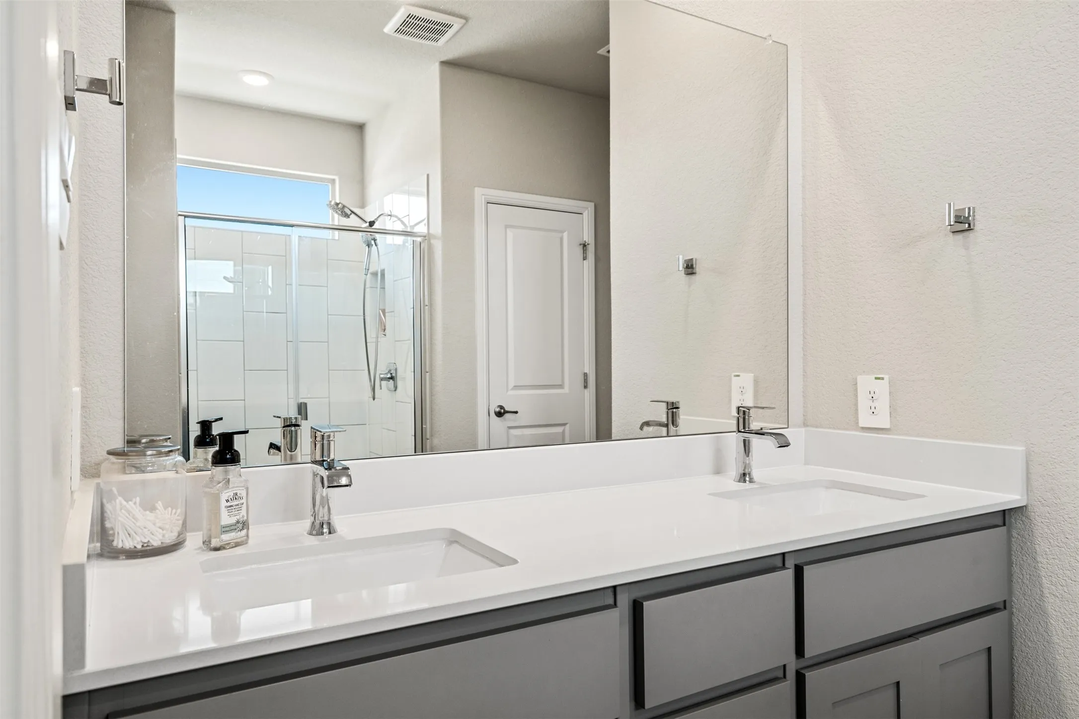 Bathroom with double vanity, a shower stall, and a textured wall