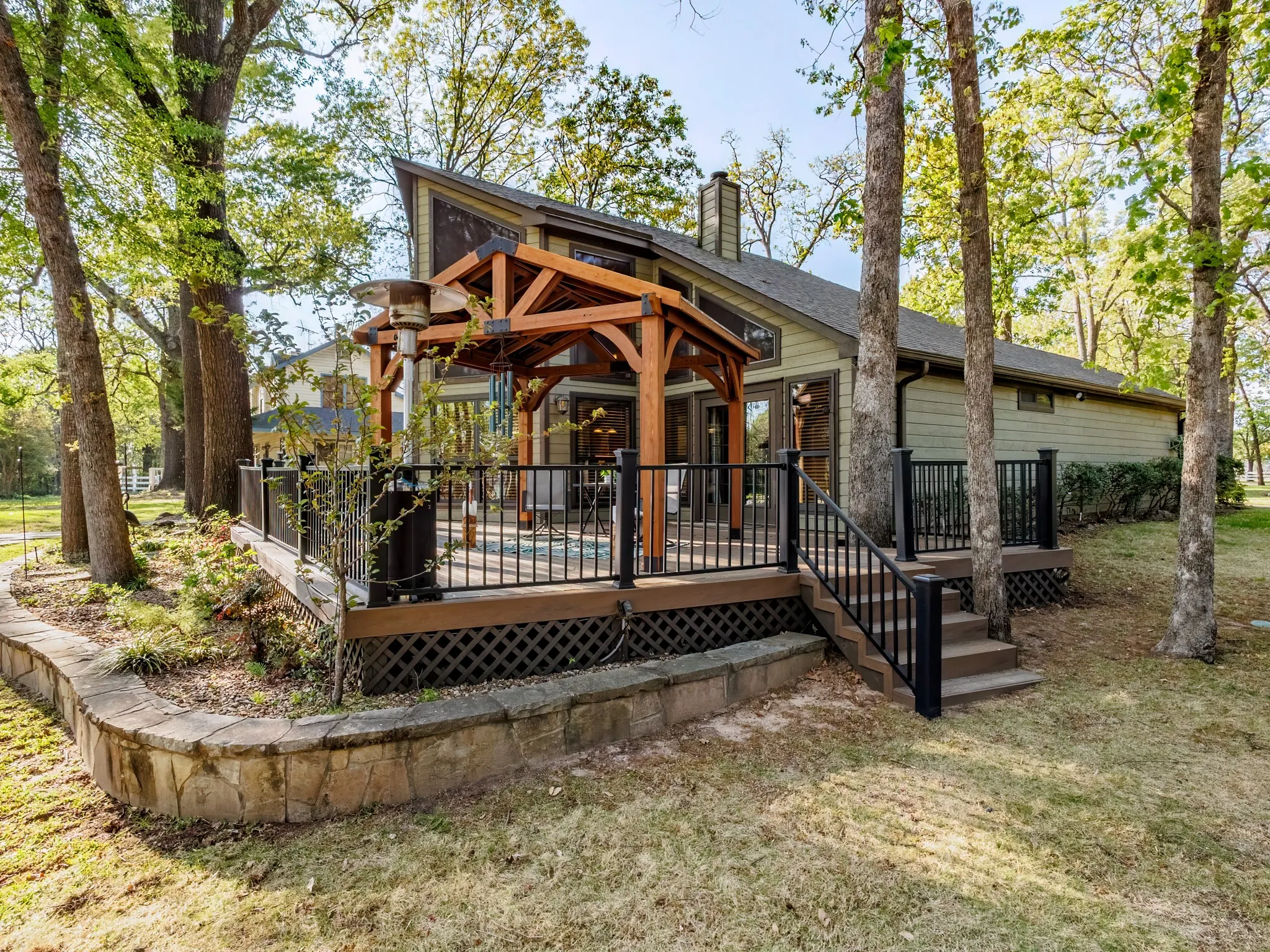 Back of house featuring a deck, a chimney, and a yard with landscaping and mature trees.