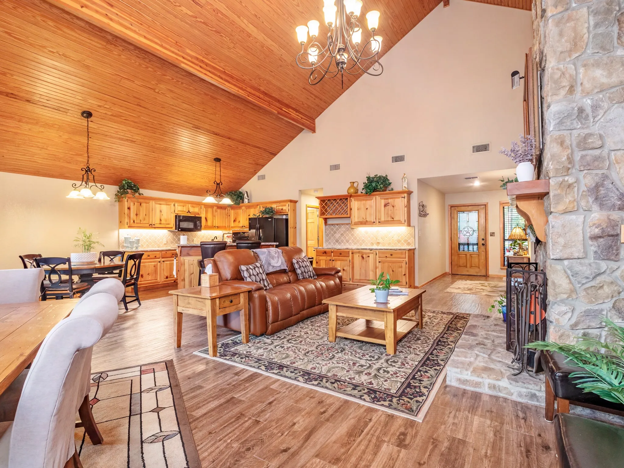 Living area featuring suspended lighting, light wood-style floors, and a high wood beamed ceiling with a view of the formal dining, breakfast nook, kitchen and foyer in the background.
