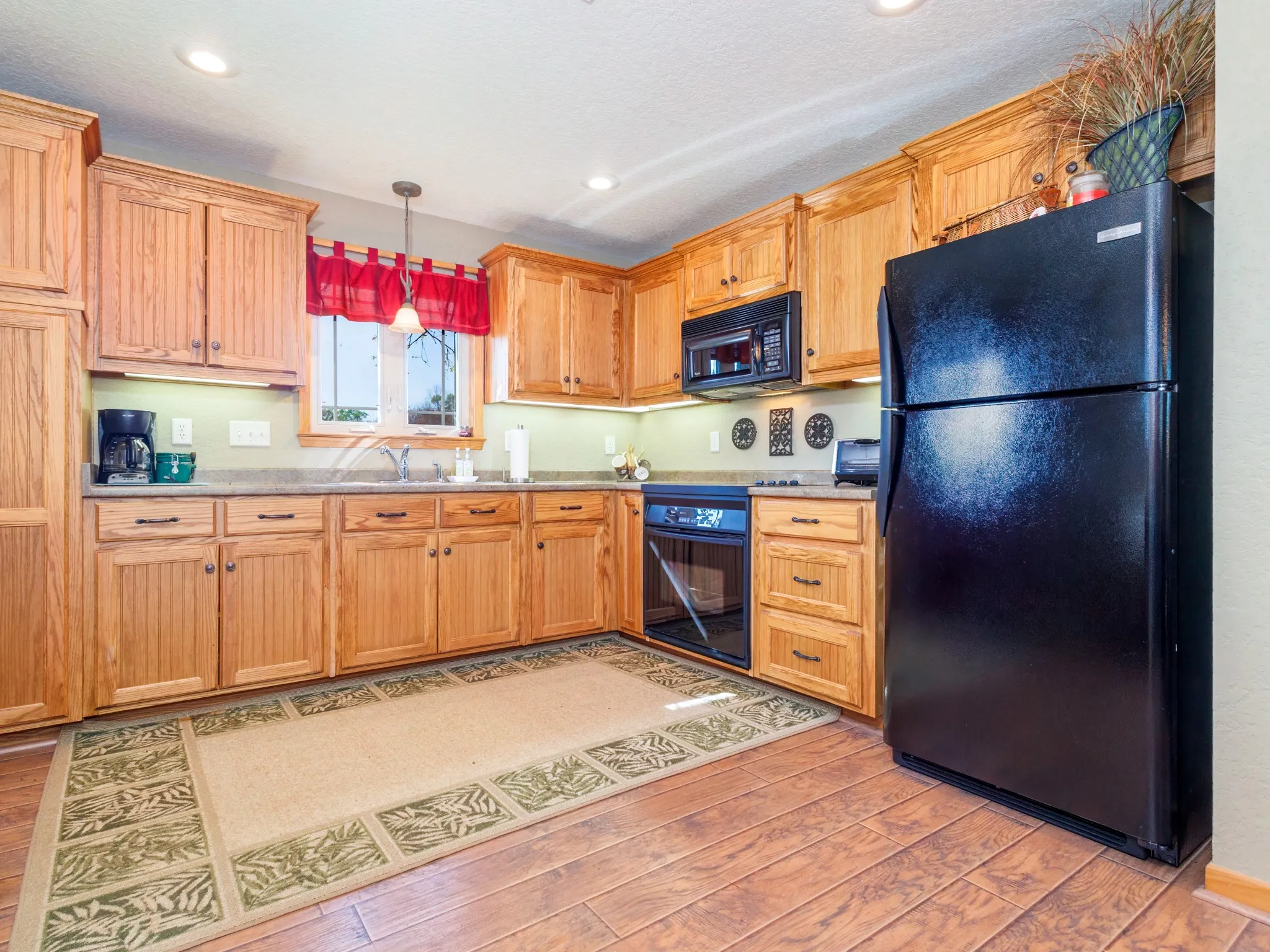 Guest Quarters Kitchen featuring black appliances, pendant lighting, light countertops, light wood-style flooring, and light wood finish cabinetry