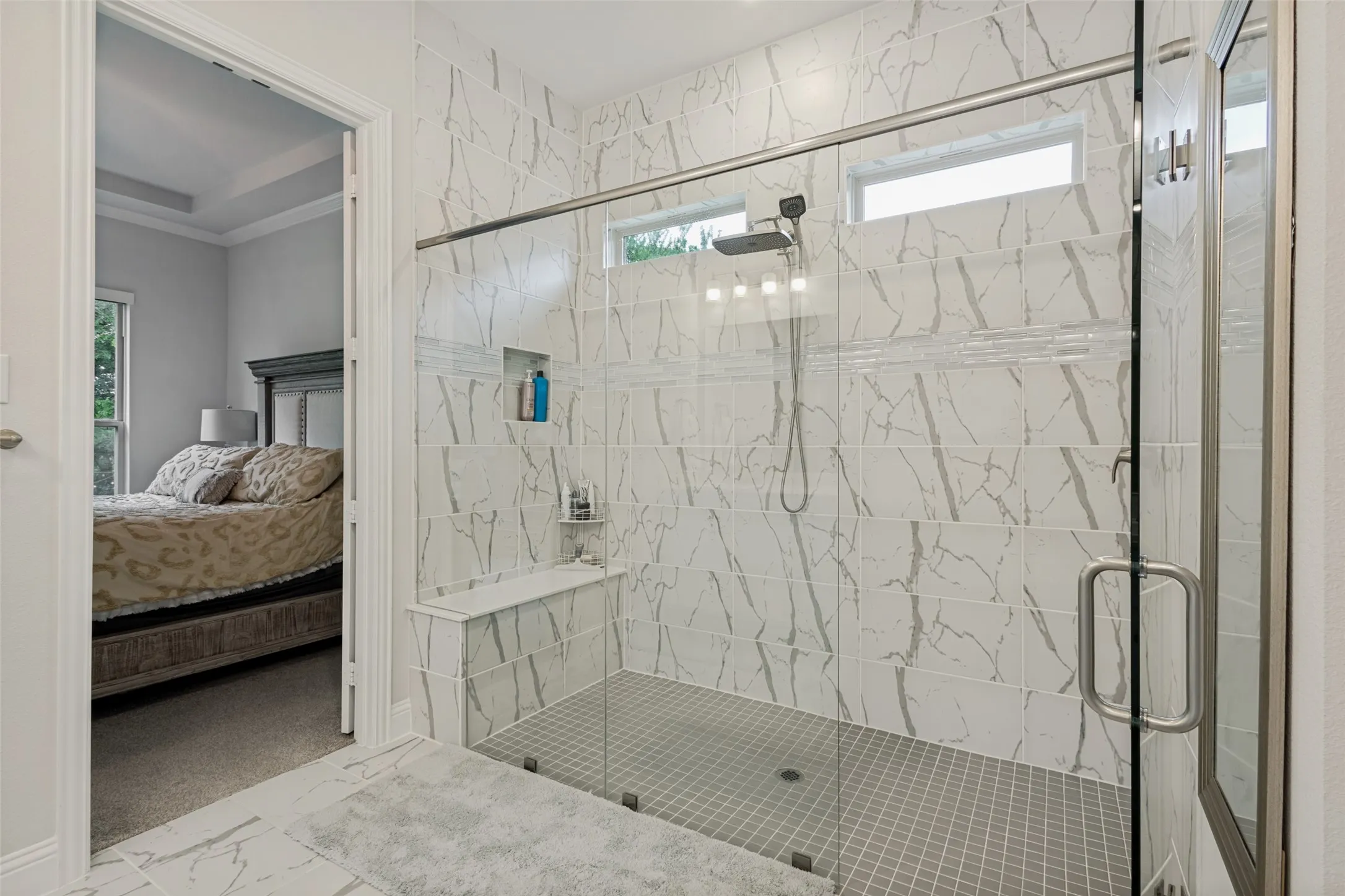 Spacious shower with glass enclosure, white marble-style wall tiles, and grey mosaic floor tiles