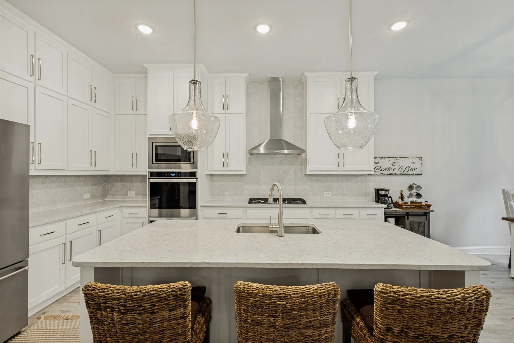 Well-appointed kitchen featuring white shaker style cabinetry, a stainless steel refrigerator, and a kitchen island with a sink and seating