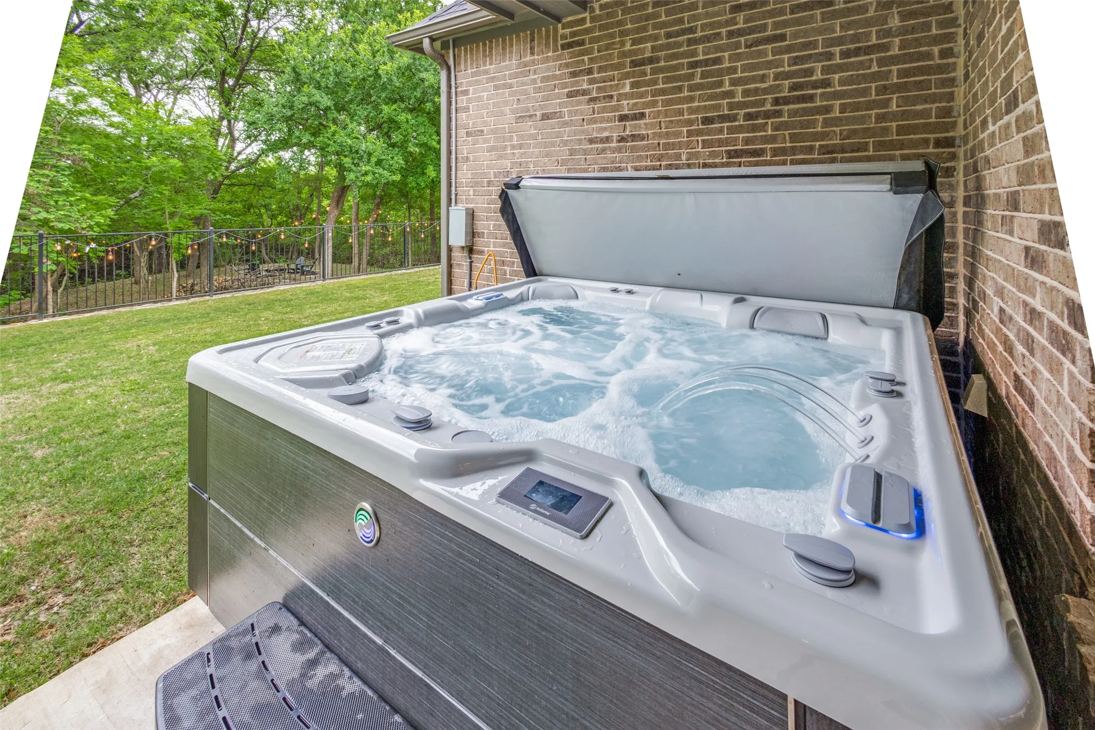 The property features an outdoor hot tub with bubbling water, set on a paved patio beside a brick wall