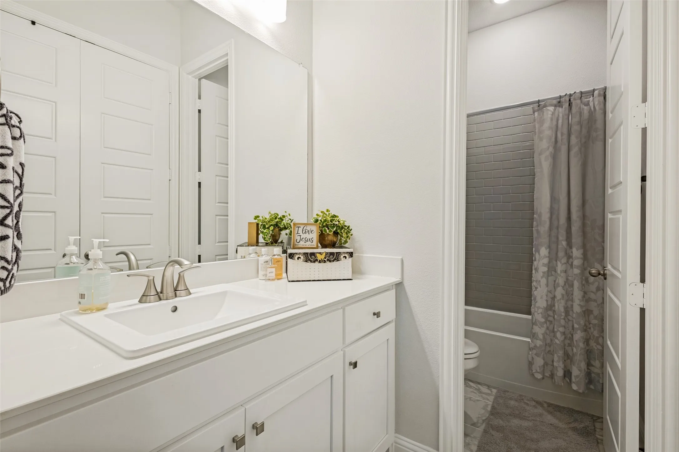 Bathroom featuring a white vanity with an integrated sink, a large mirror, and a shower with gray subway tile surround