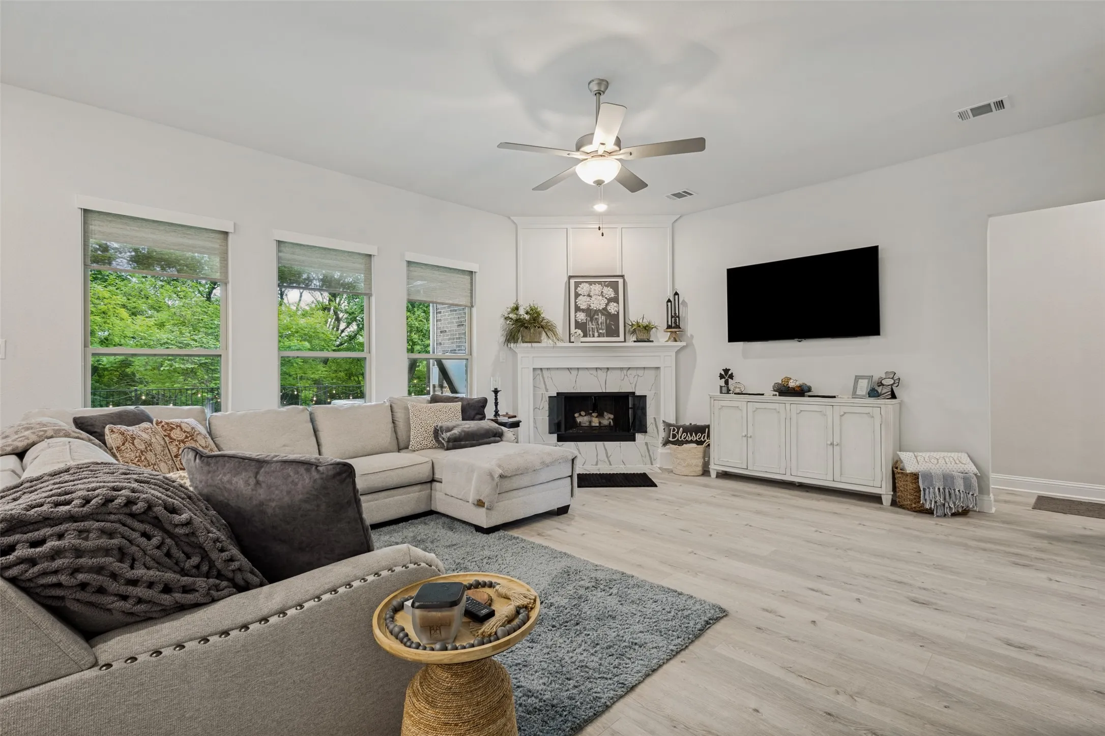 The living room features light-colored flooring, a corner fireplace with a mantel, and three windows providing natural light