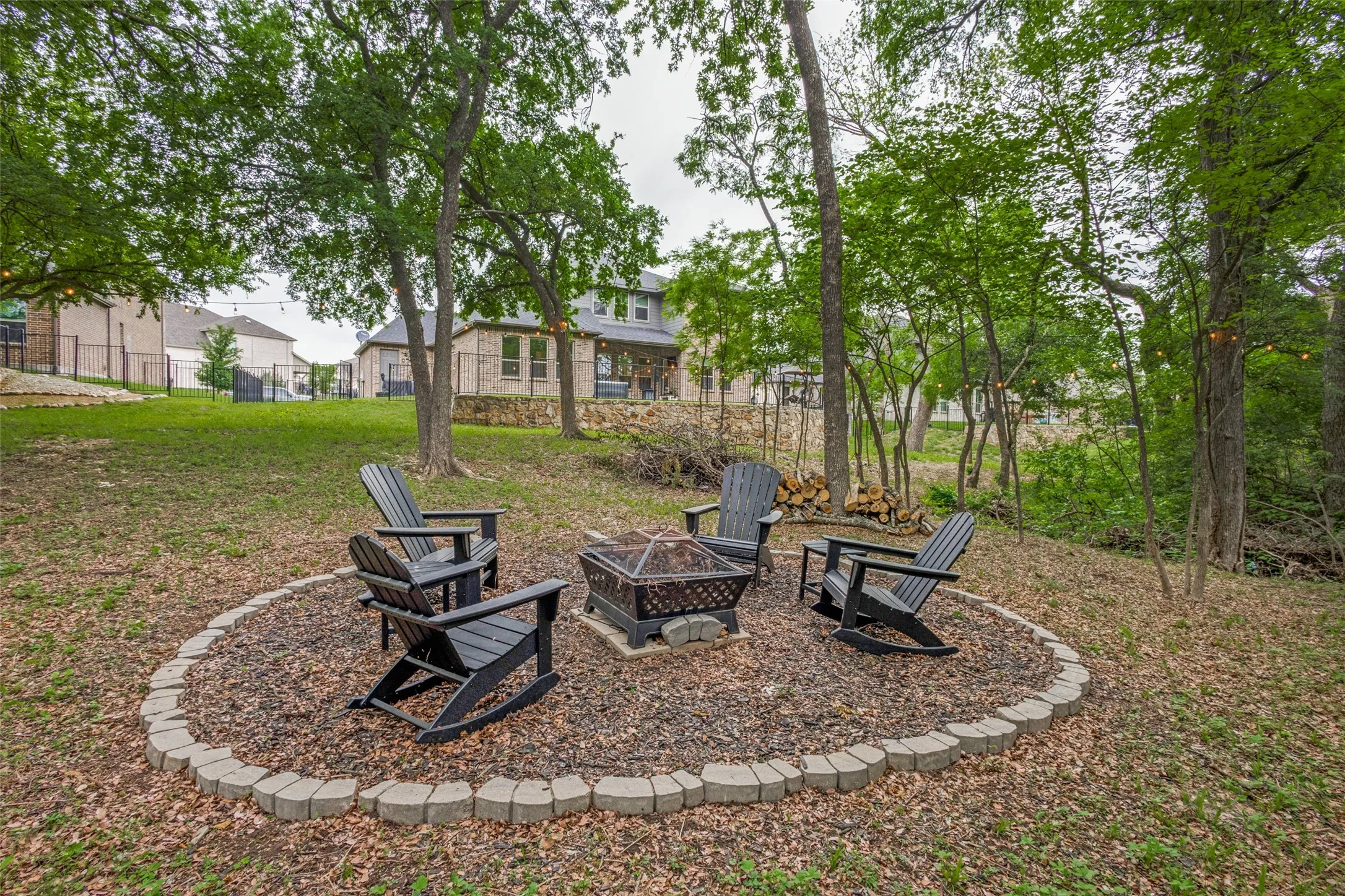 The property features a fire pit area with pavers, surrounded by four dark outdoor chairs