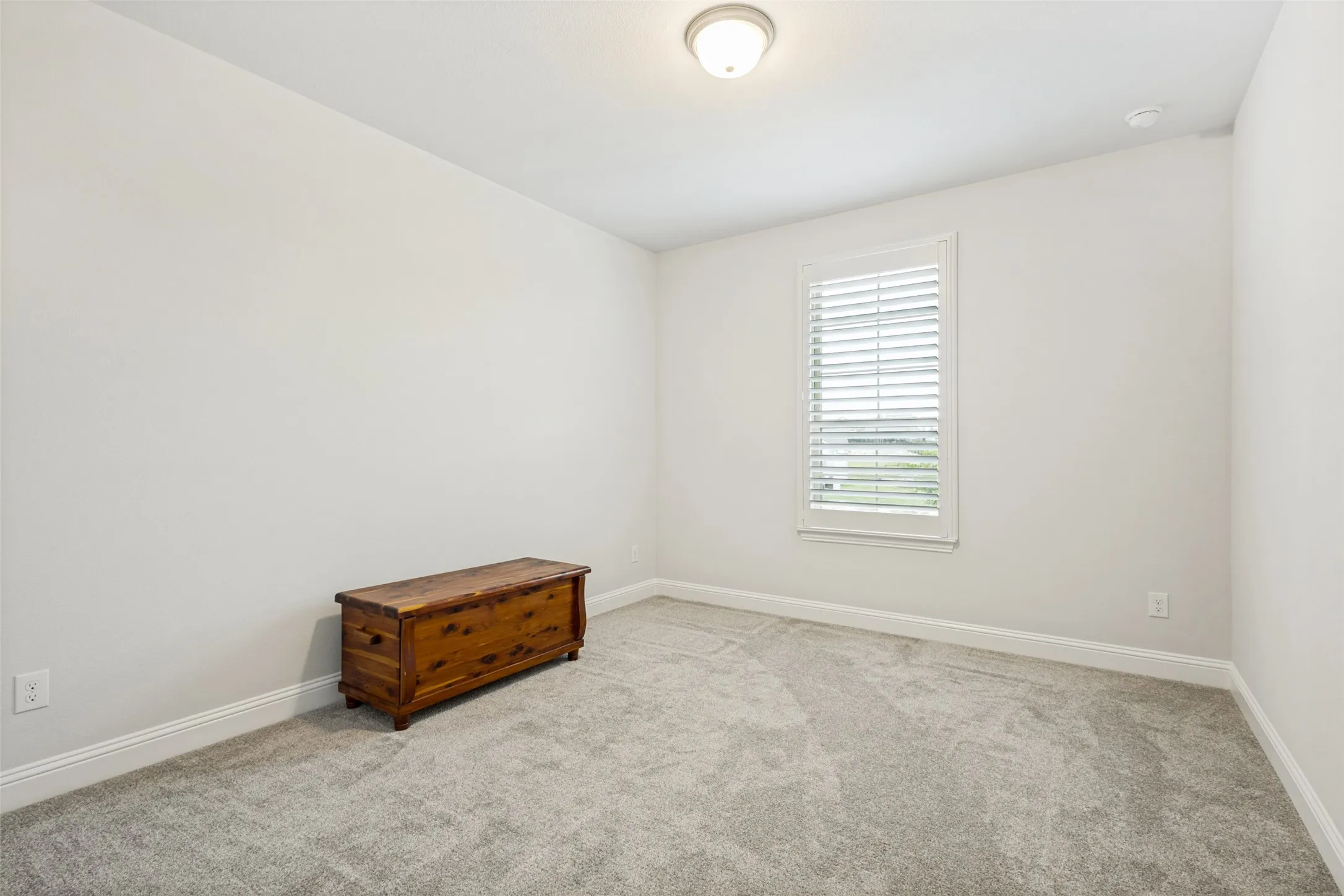 This room features light-colored walls and carpeting, a window with white blinds, and a ceiling light​​‌​​​​‌​​‌‌​‌‌​​​‌‌​‌​‌​‌​​​‌​​ fixture