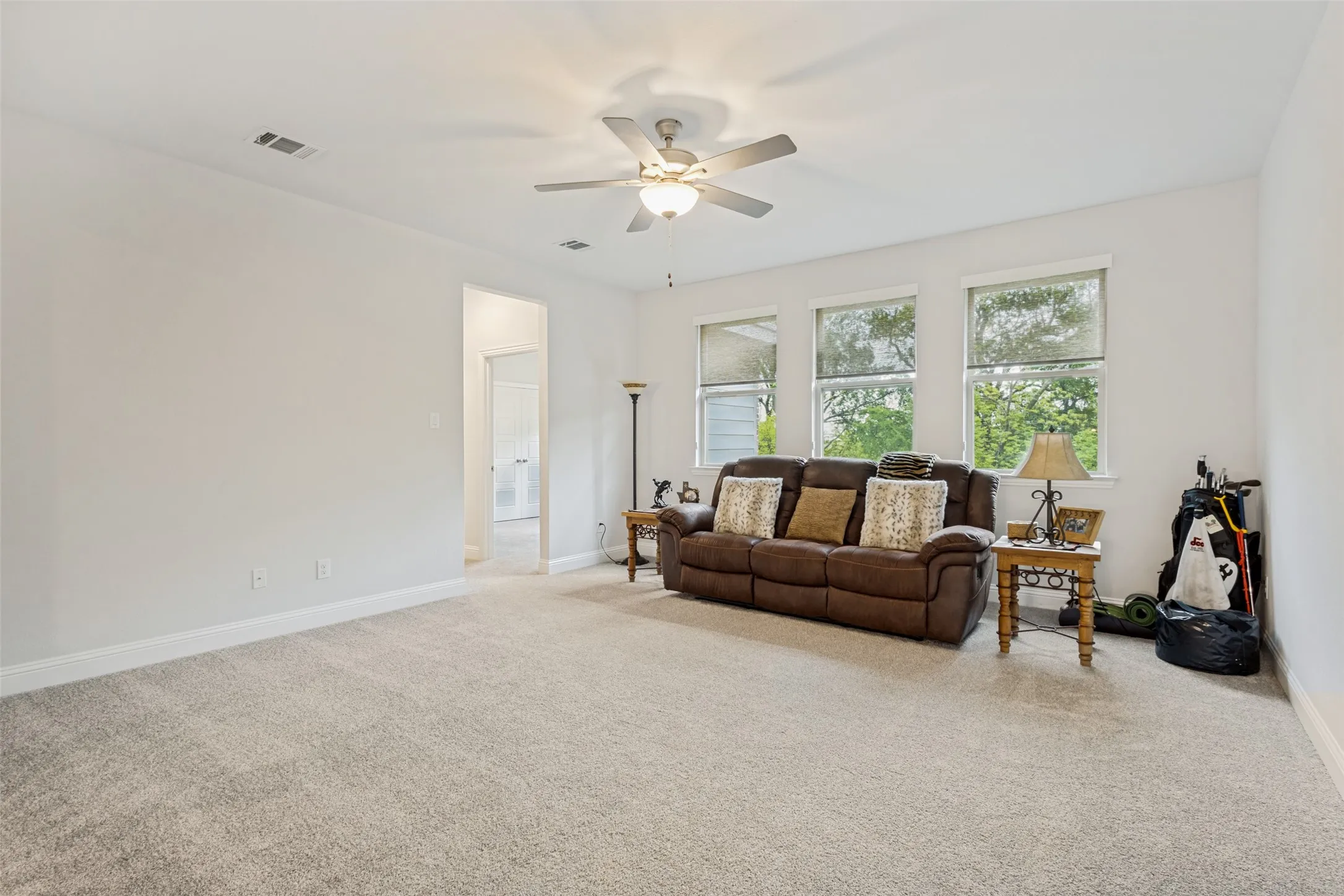 Spacious living area featuring light-colored carpeting, white walls, and a ceiling fan with integrated lighting