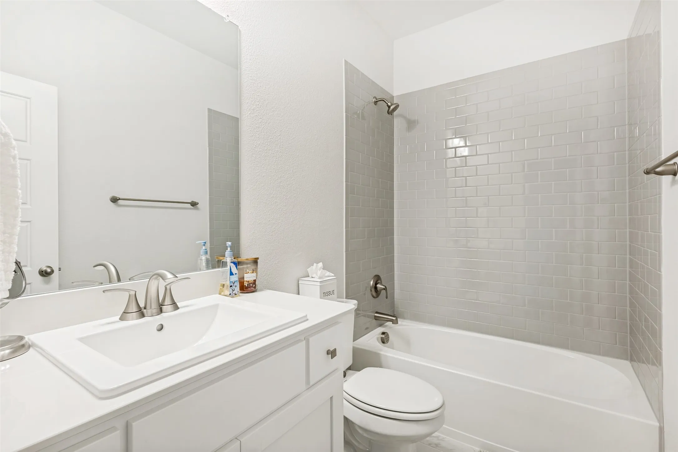 This bathroom features a white vanity with a rectangular sink and brushed nickel faucet, a toilet, and a bathtub with subway tile surround