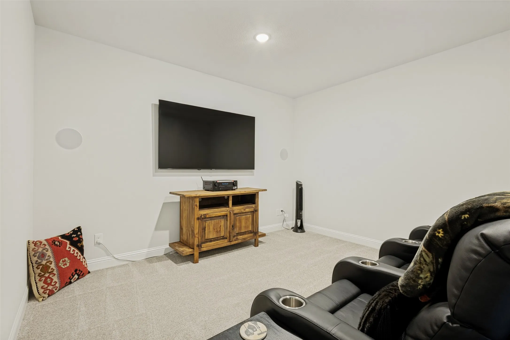 This room features light-colored carpet, recessed lighting, and wall-mounted speakers