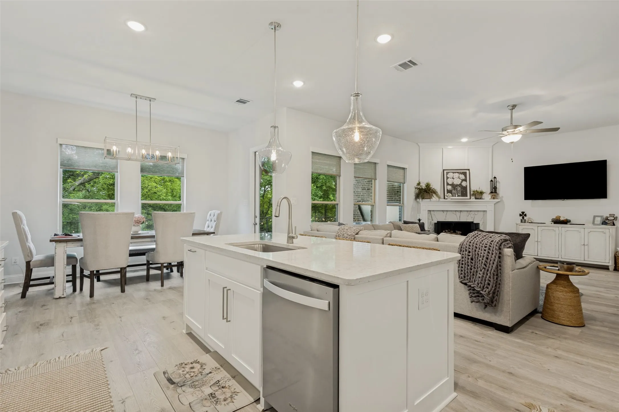 The open concept living area features light-colored flooring, a kitchen island with a sink and built-in dishwasher, and recessed lighting throughout