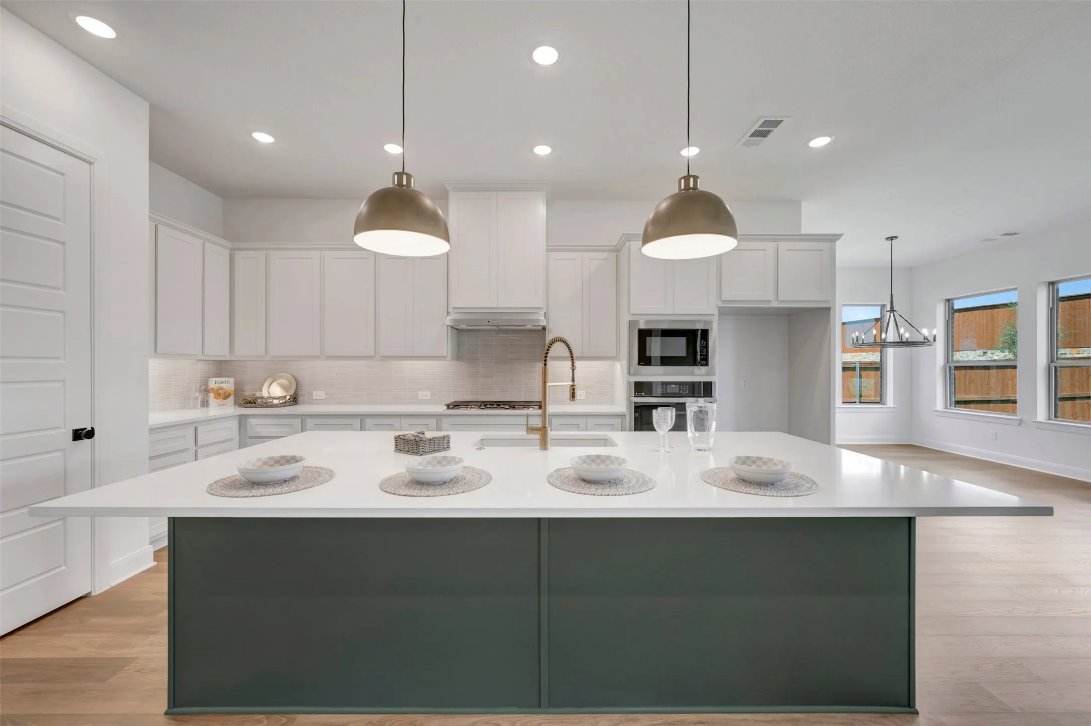 Modern kitchen featuring a dual-island layout with a contrasting dark green base and white quartz countertops, paired with brass pendant lighting
