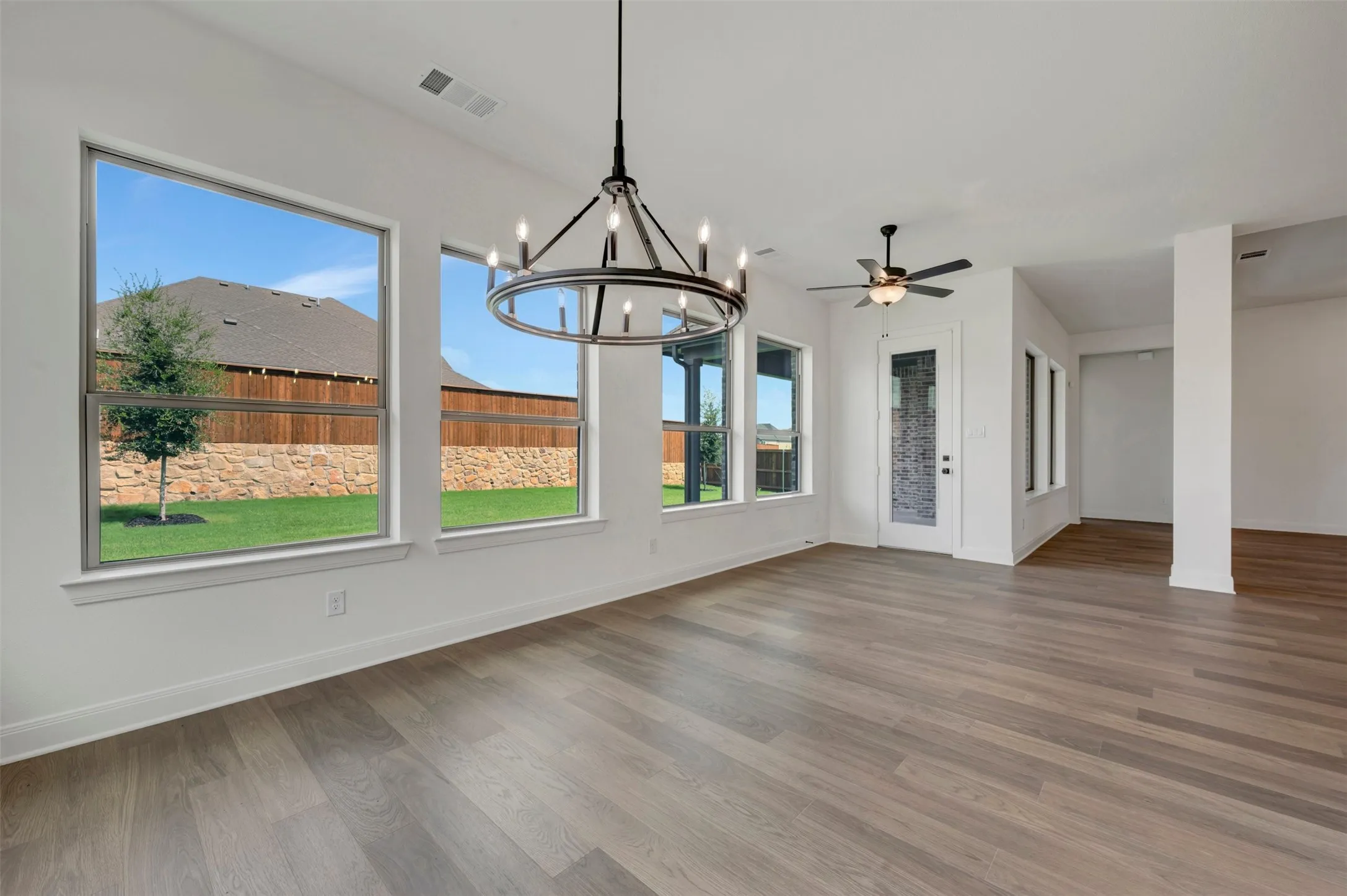 Wood-finish flooring throughout, bright interior with multiple windows, contemporary chandelier, ceiling fan, and white trim