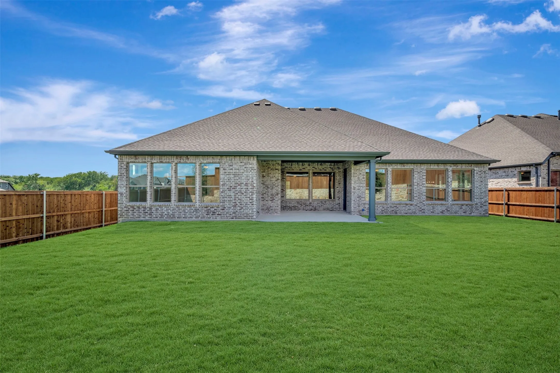 Expansive green lawn, covered patio, brick exterior, multiple windows, and a wood privacy fence
