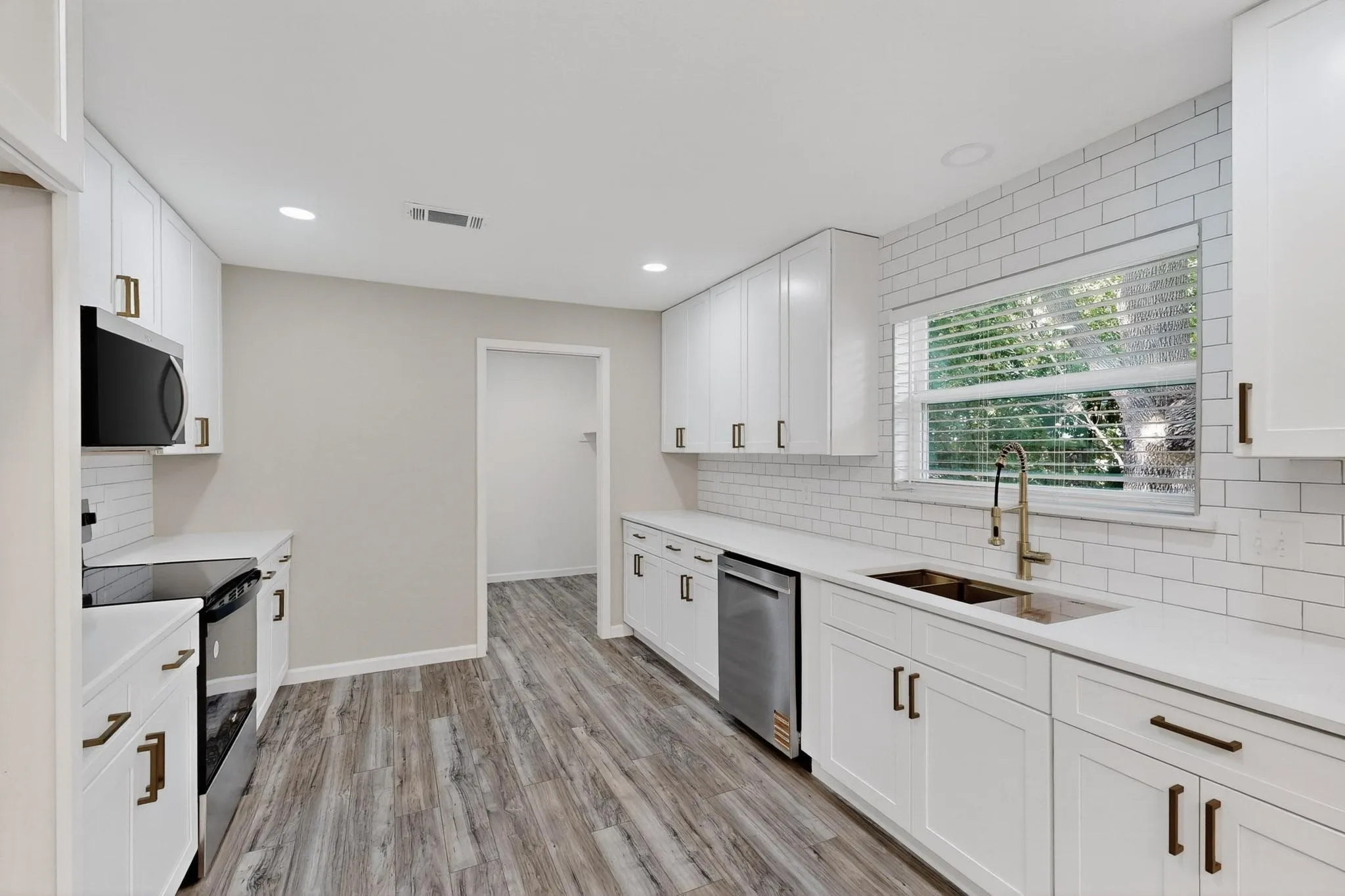 Kitchen featuring stainless steel appliances, white cabinets, light wood-style flooring, light stone counters, and recessed lighting
