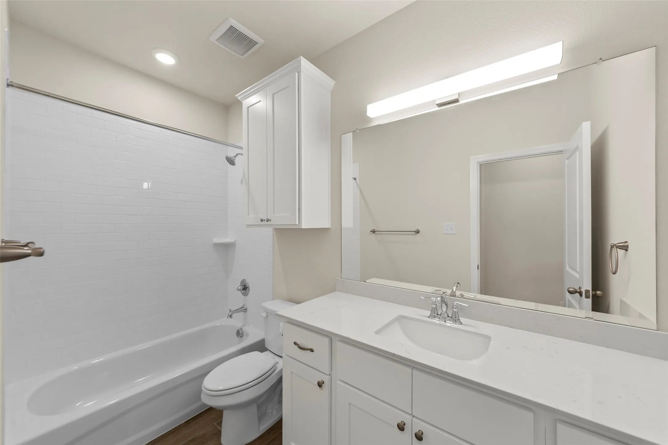 Bathroom featuring a white subway tile shower surround, a built-in white cabinet, a full-width mirror, a vanity with a white countertop and integrated sink, and wood-finish flooring