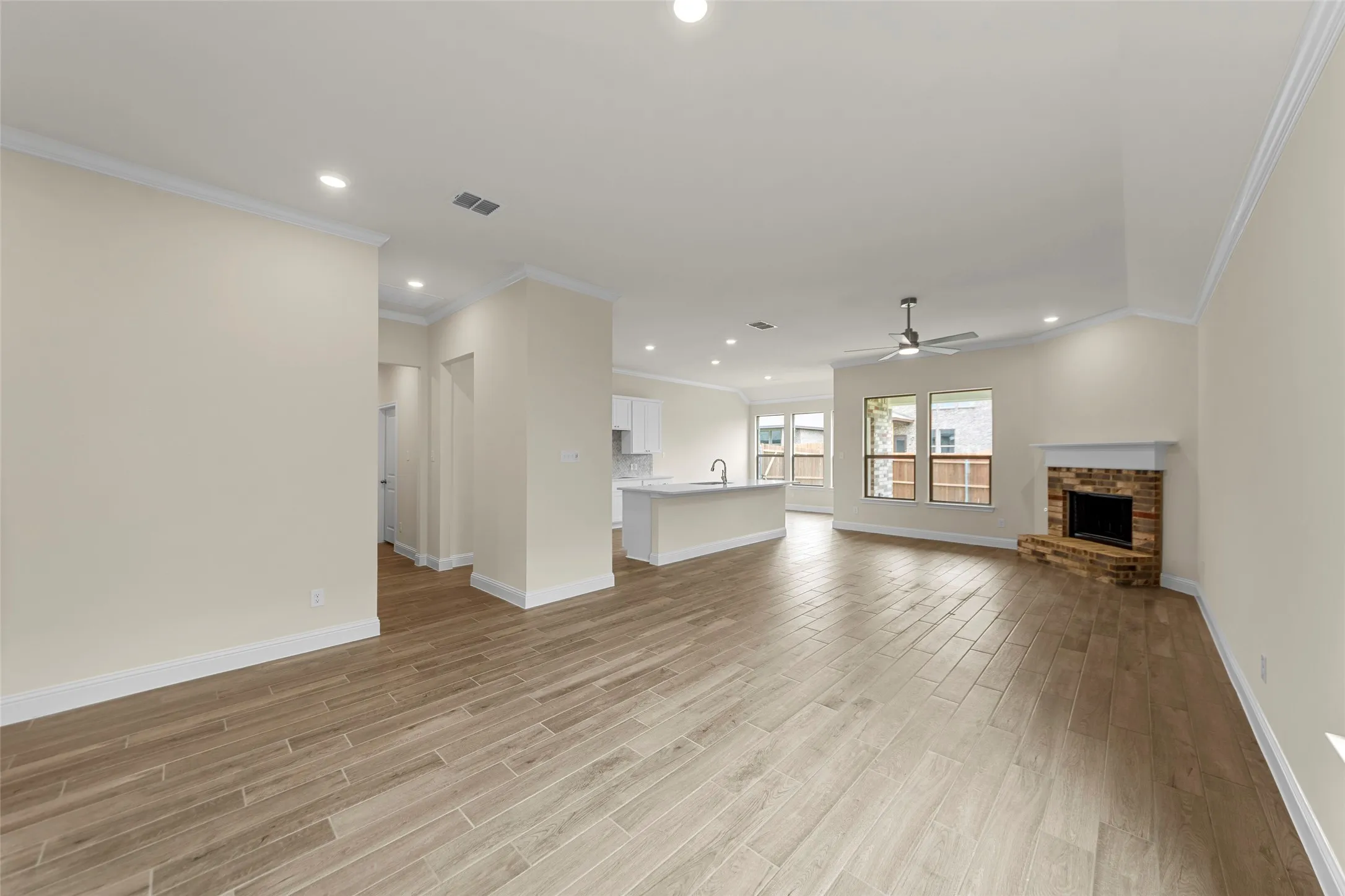 Spacious living area featuring wood-finish flooring, recessed lighting, and a brick fireplace with a white mantel
