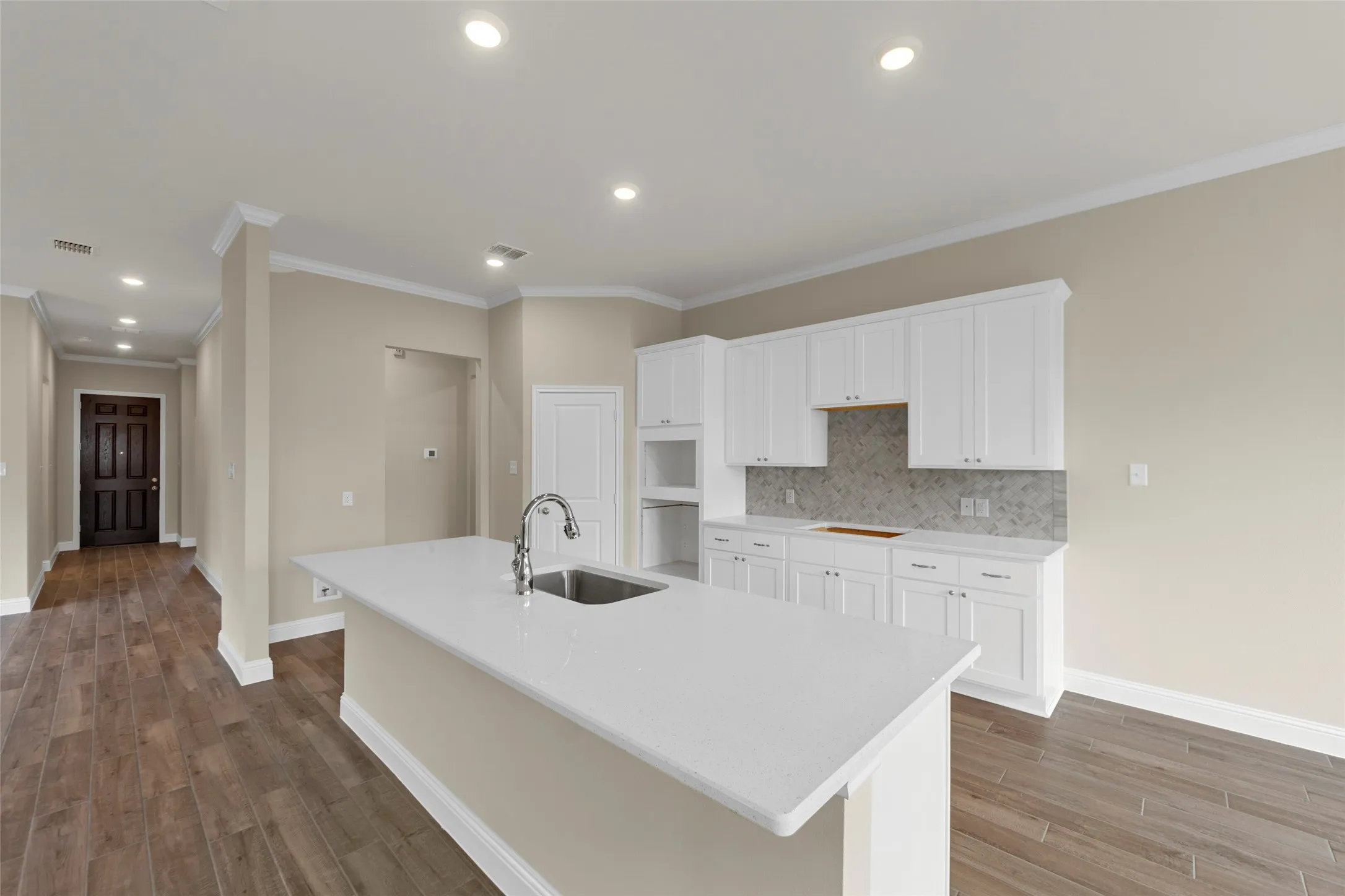 Bright kitchen featuring white cabinetry, a large center island with an undermount sink, quartz countertops, a tiled backsplash, and recessed lighting