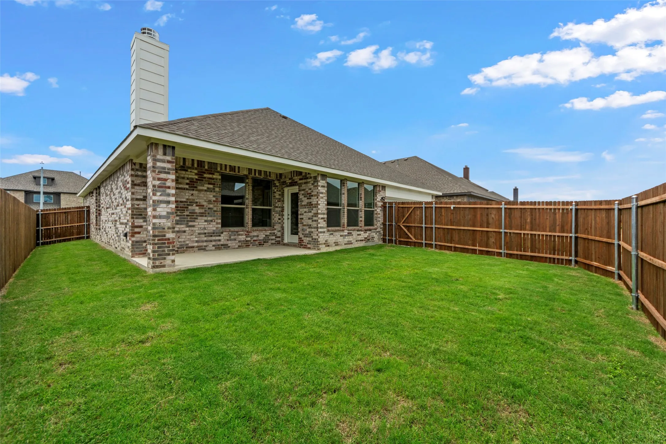 Expansive backyard featuring a manicured lawn, full perimeter privacy fencing, covered patio, and a multi-tone brick exterior with a prominent chimney structure