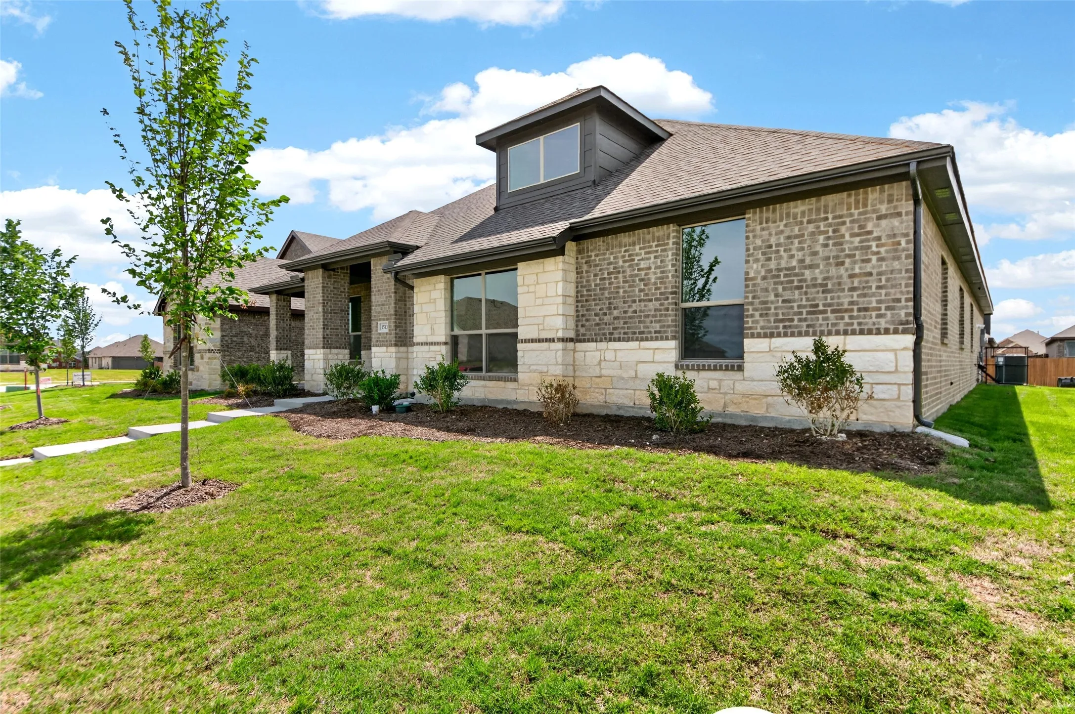 Stone and brick exterior with a dormer window, composition shingle roof, and a concrete walkway
