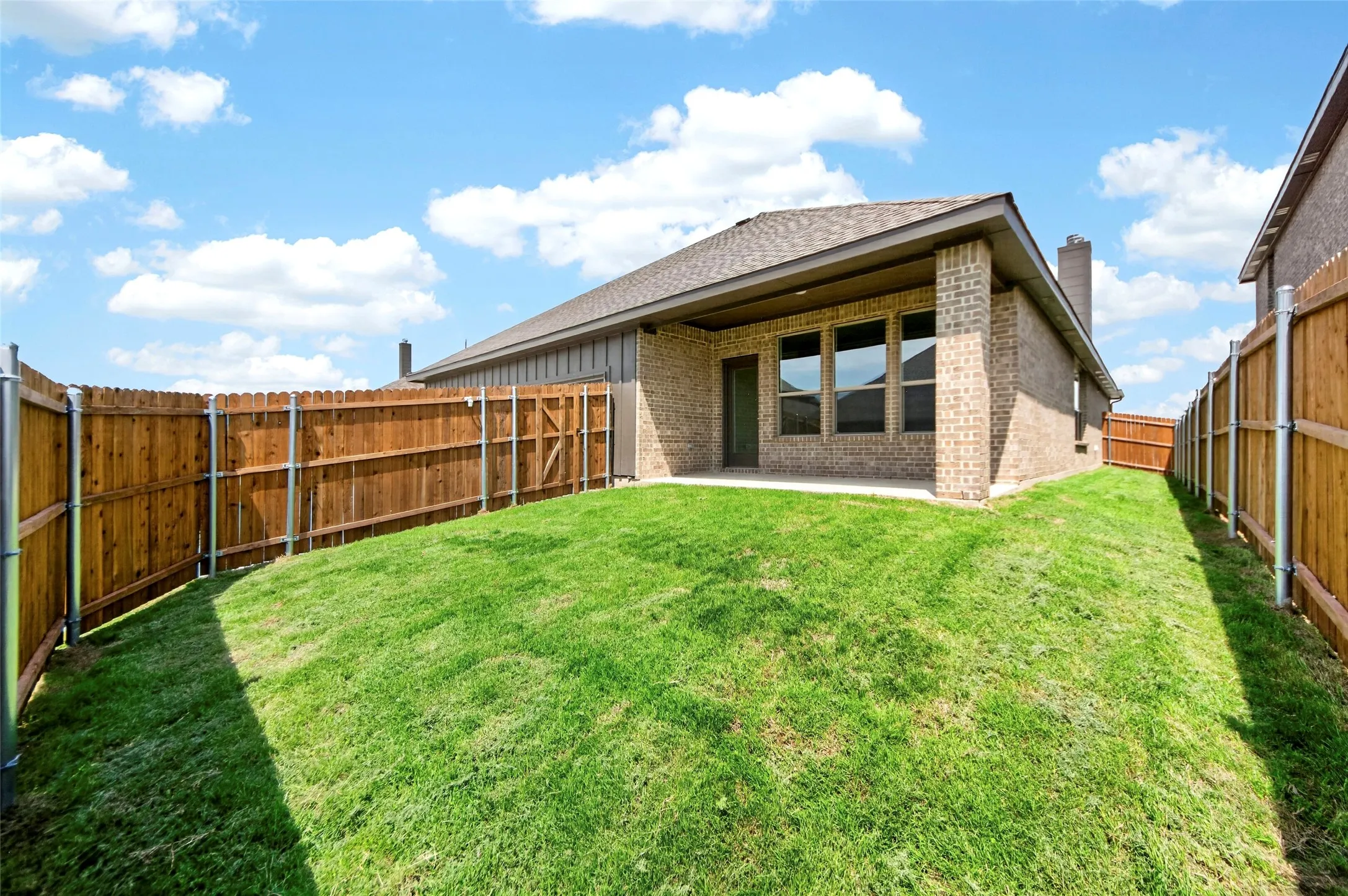 Expansive backyard featuring a manicured lawn, full privacy fencing, and a covered patio