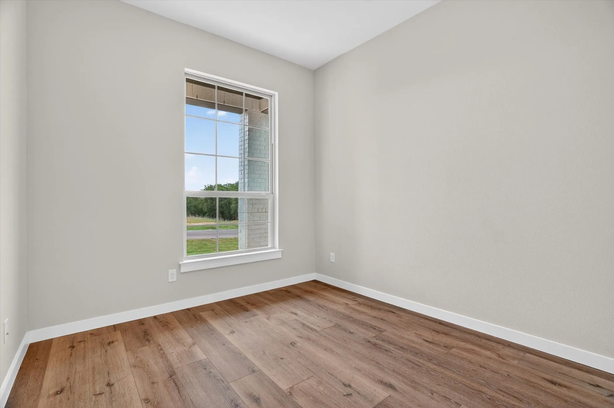 Spacious room featuring wood-finish flooring, light gray wall paint, and white trim
