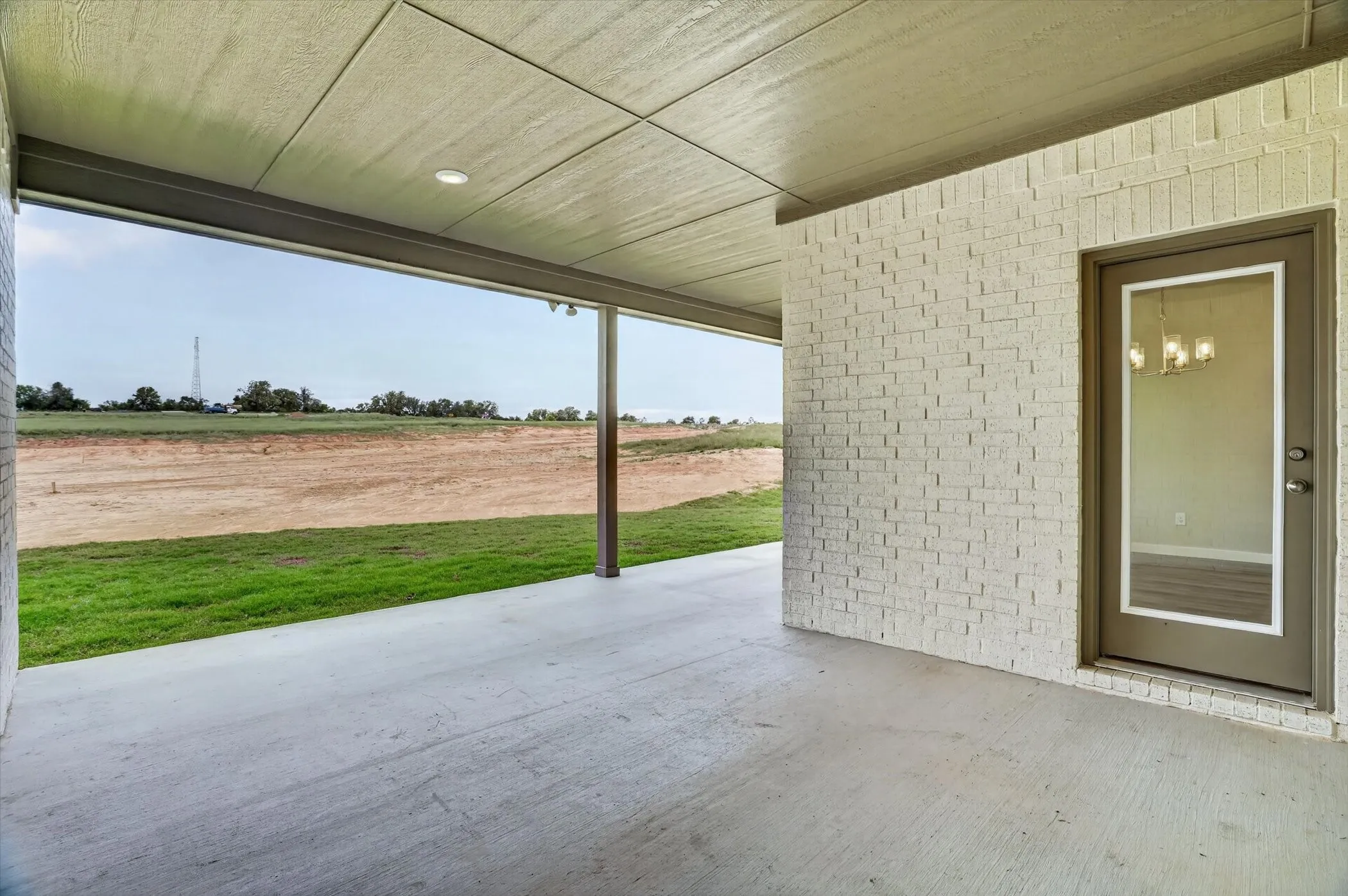 Covered patio with a concrete surface, featuring a light-colored brick exterior wall, recessed lighting, and a glass-paneled door