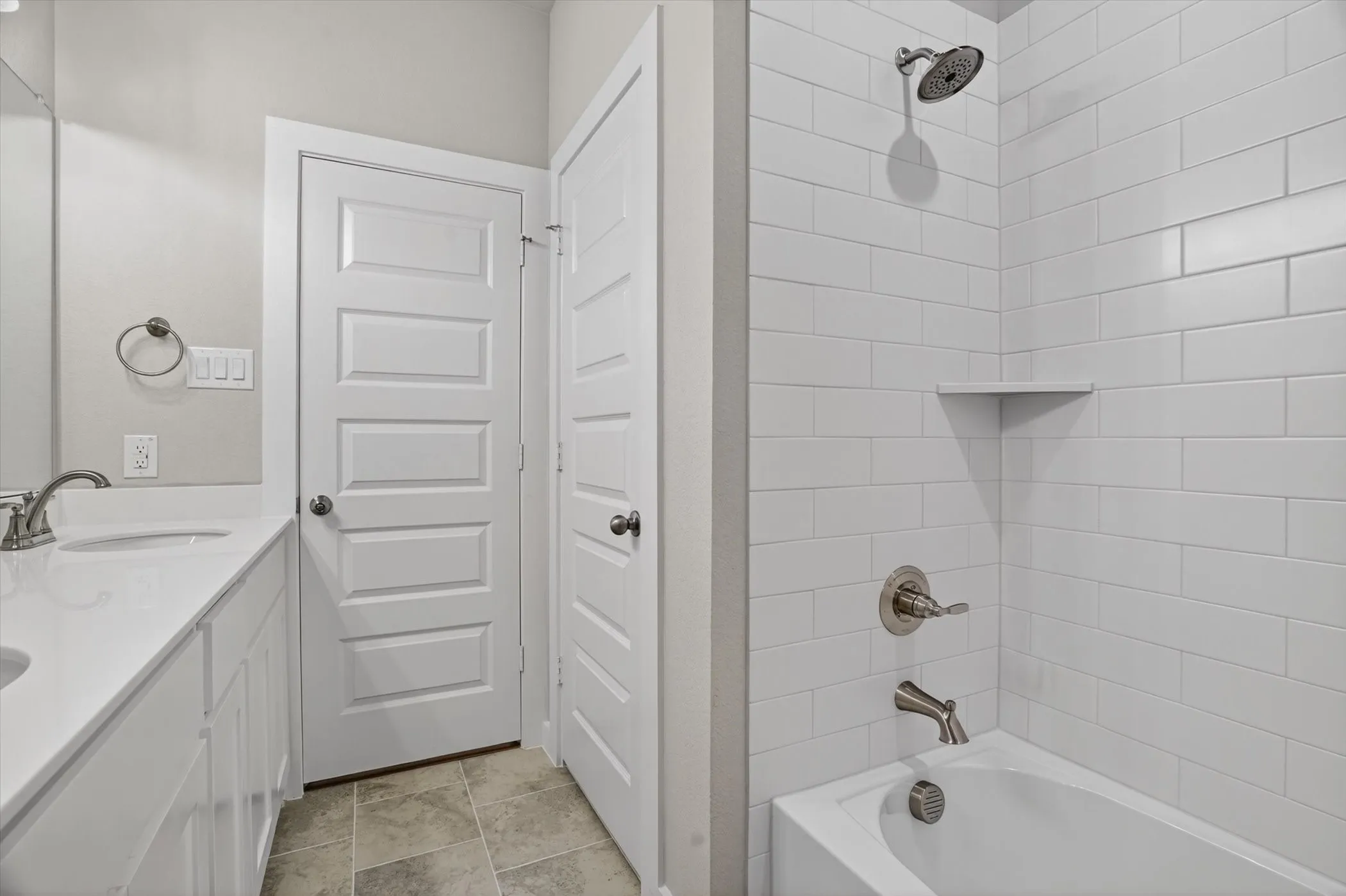 Full bathroom featuring a white subway tile tub surround with an integrated corner shelf, brushed nickel fixtures, a white vanity with an undermount sink, and a coordinating countertop