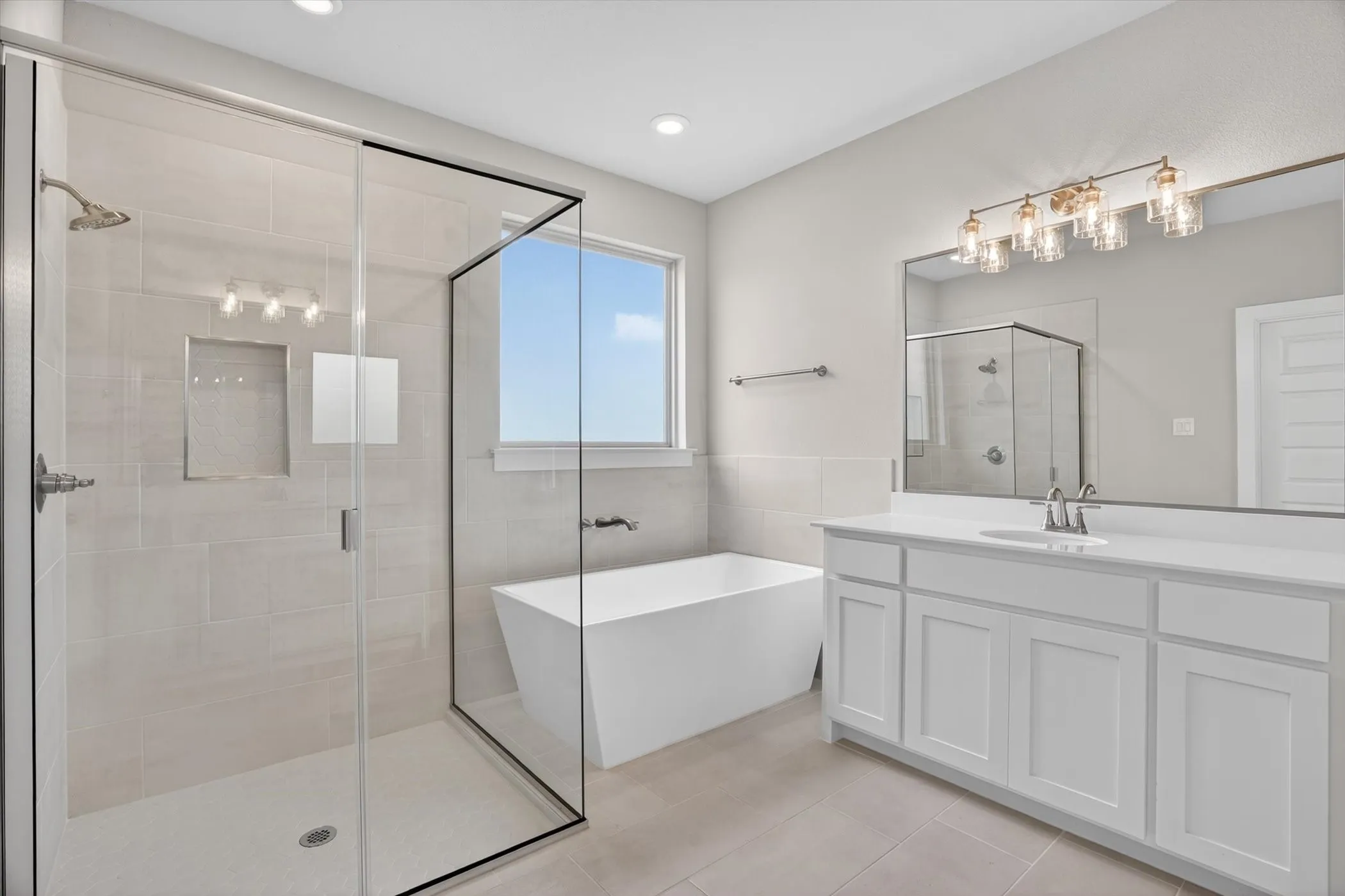 Contemporary bathroom featuring a frameless glass shower enclosure, a freestanding soaking tub, a double vanity with white cabinetry, a large wall-mounted mirror, and tile flooring
