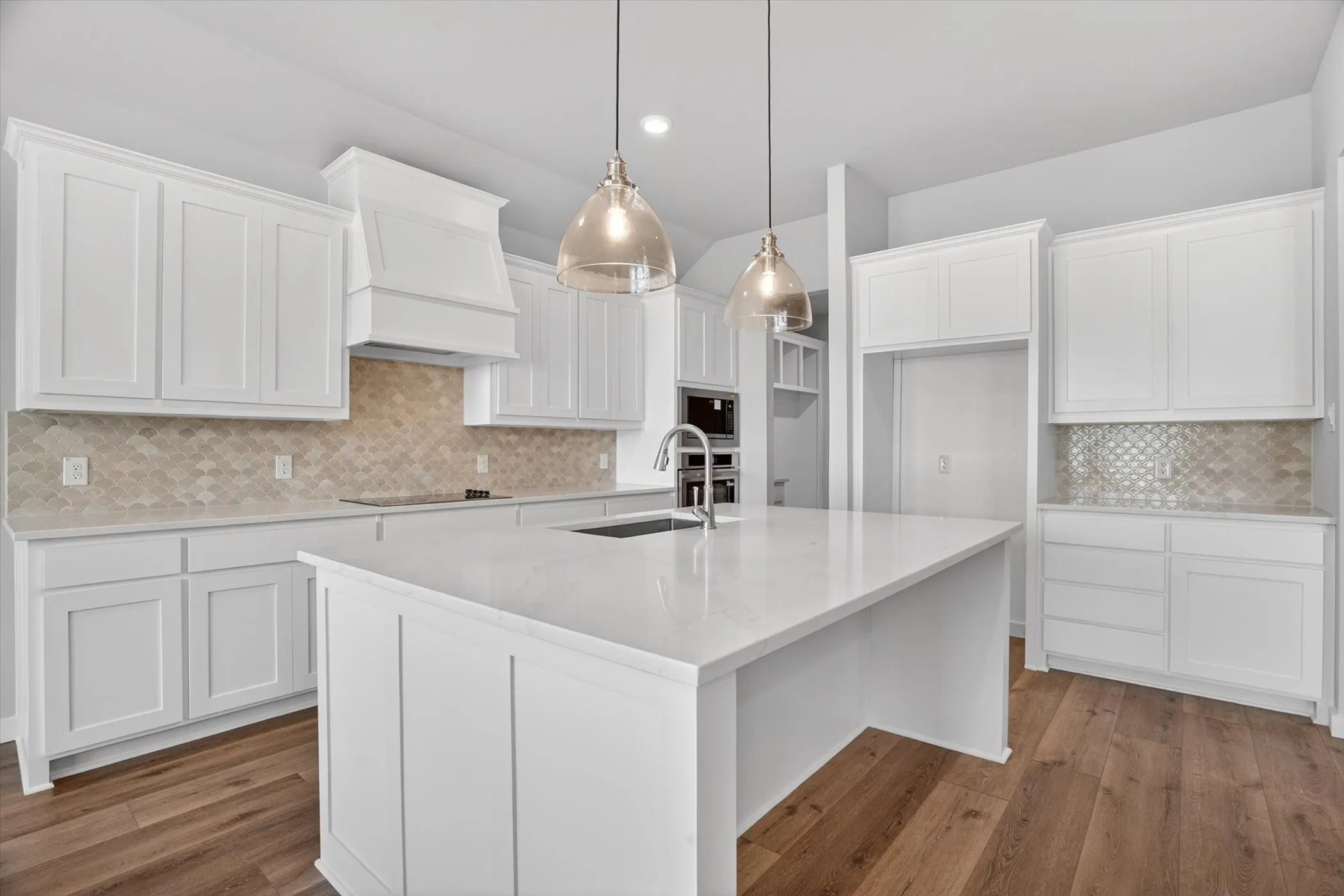 Kitchen featuring a large central island with a sink, white cabinetry, integrated stainless steel appliances, and wood-finish flooring