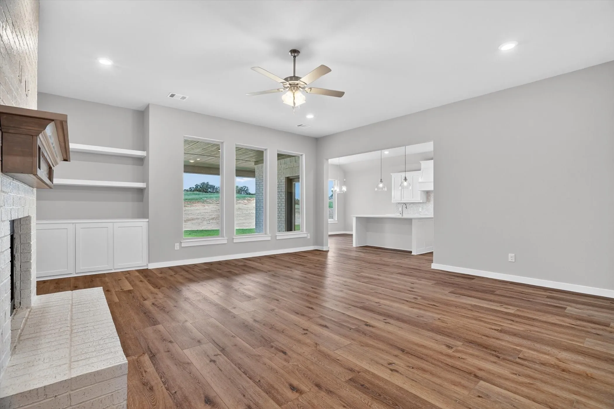 Spacious interior with wood-finish flooring, a white brick fireplace with a wood mantle, and built-in shelving with cabinetry