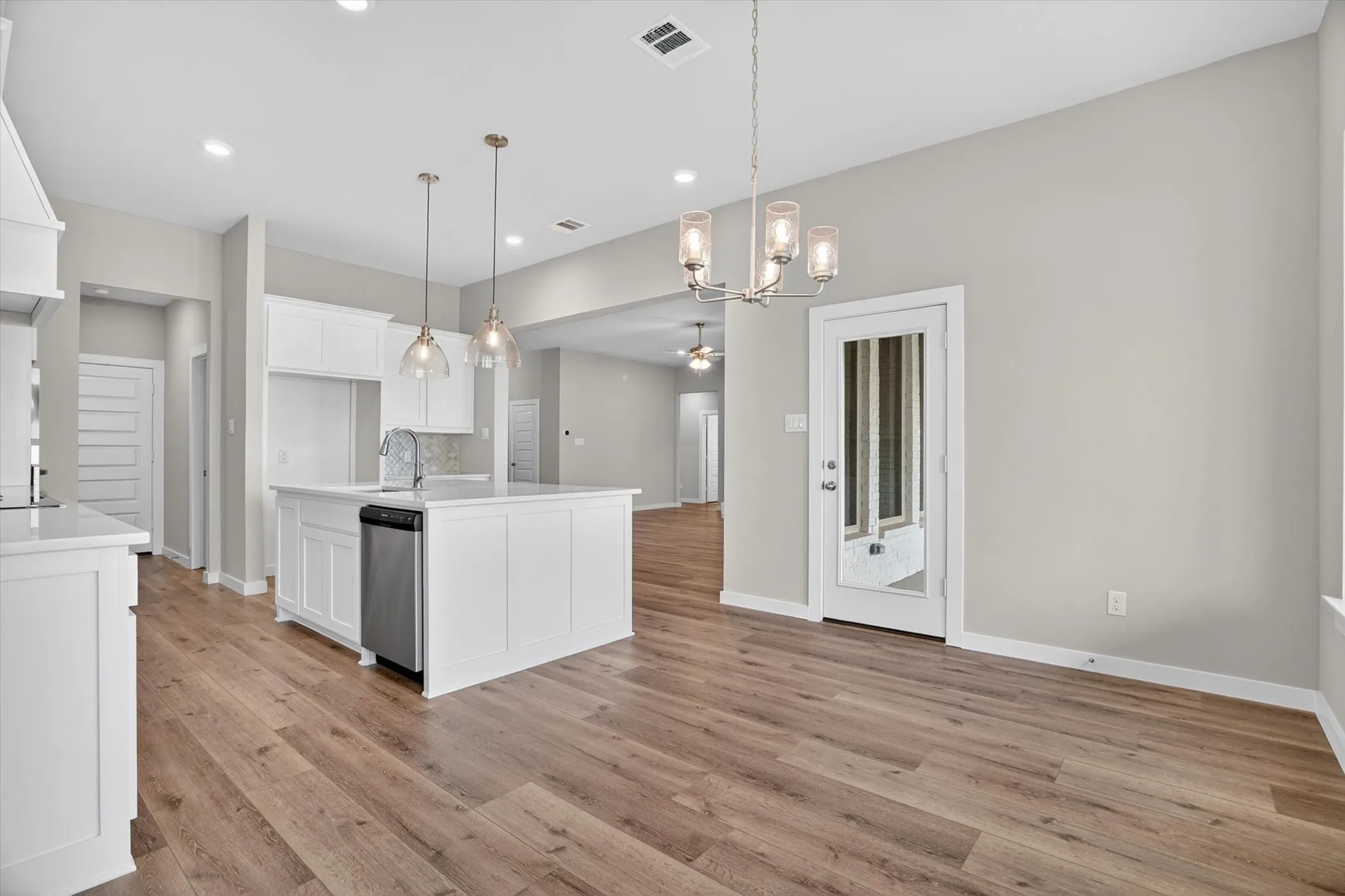 Open-concept kitchen and dining area featuring wood-finish flooring, white cabinetry, a kitchen island with a built-in sink, and pendant lighting