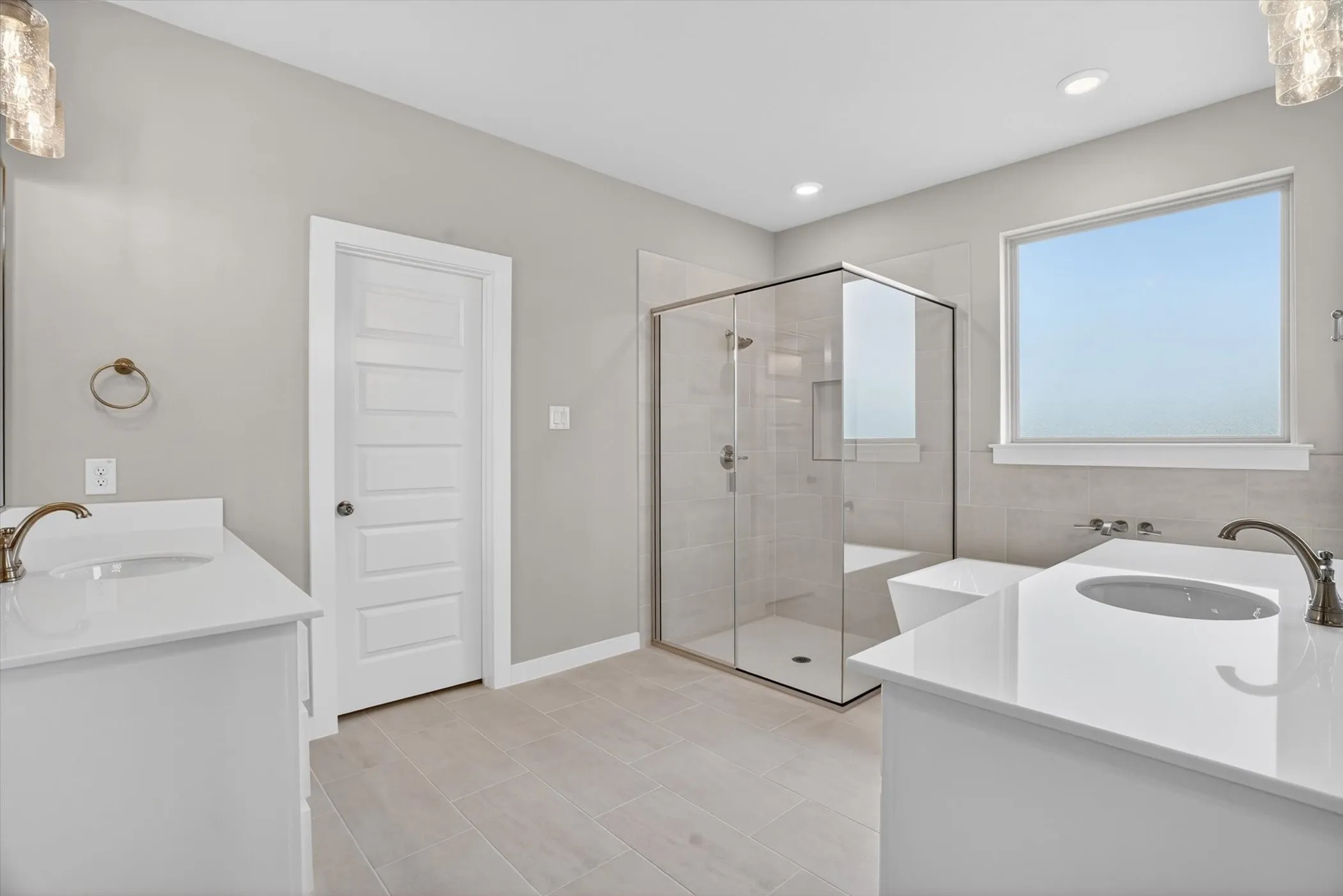 Bathroom featuring dual vanities with white countertops, a frameless glass shower enclosure, a built-in bathtub, and light tile flooring