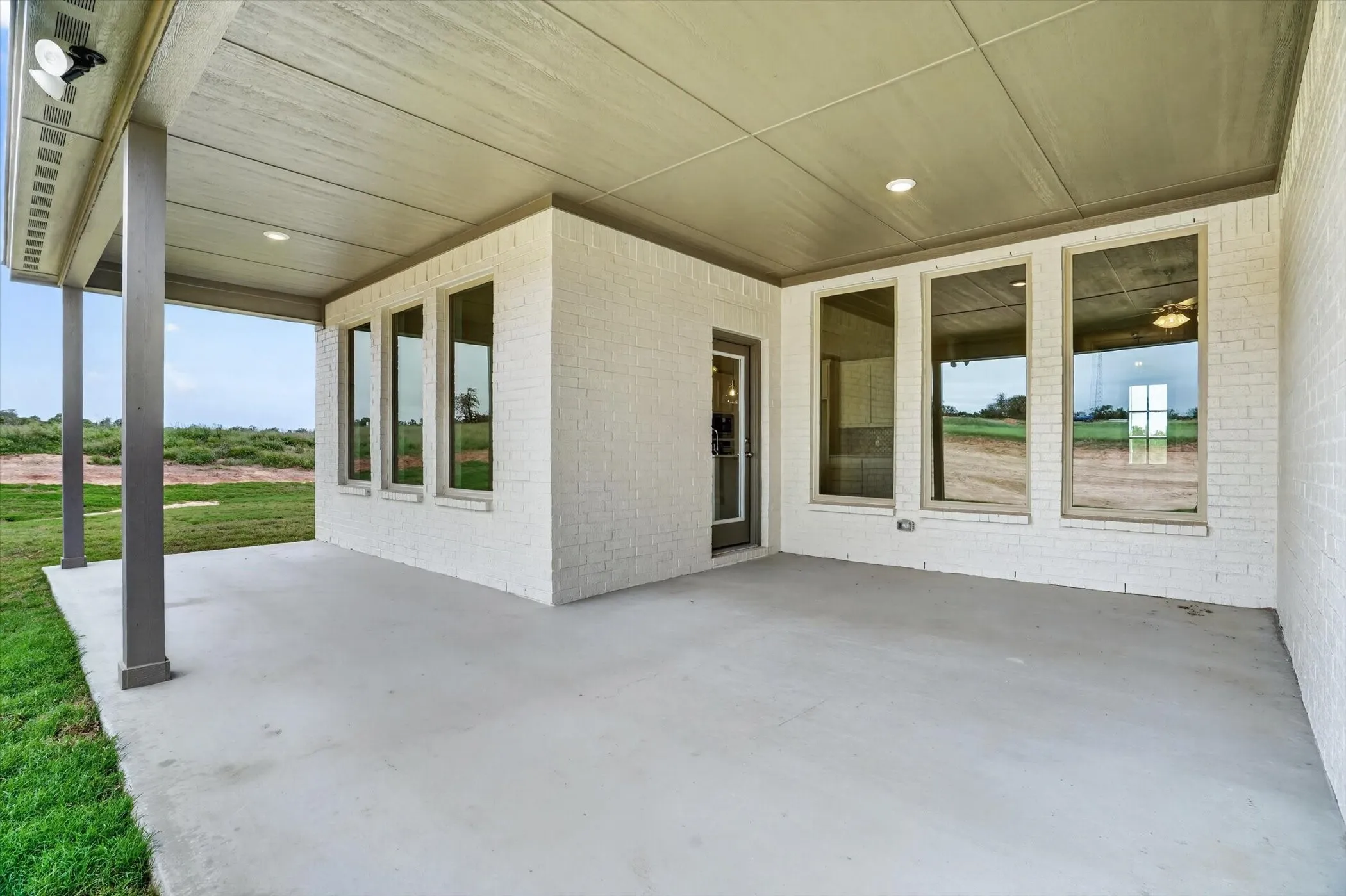 Covered patio featuring a concrete surface, white brick exterior, recessed lighting, and expansive windows