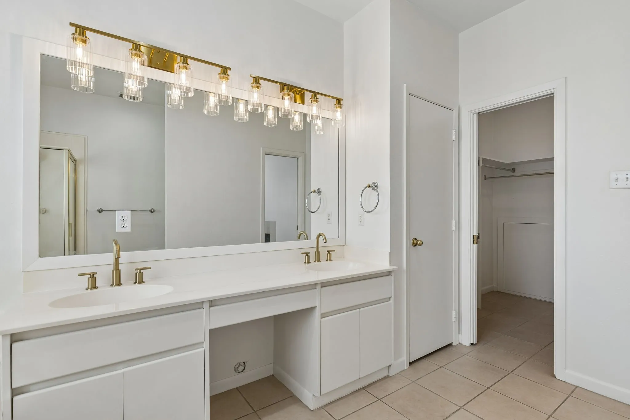 Primary bathroom featuring double vanity, looking into the large walk in closet, linen closet on the left.