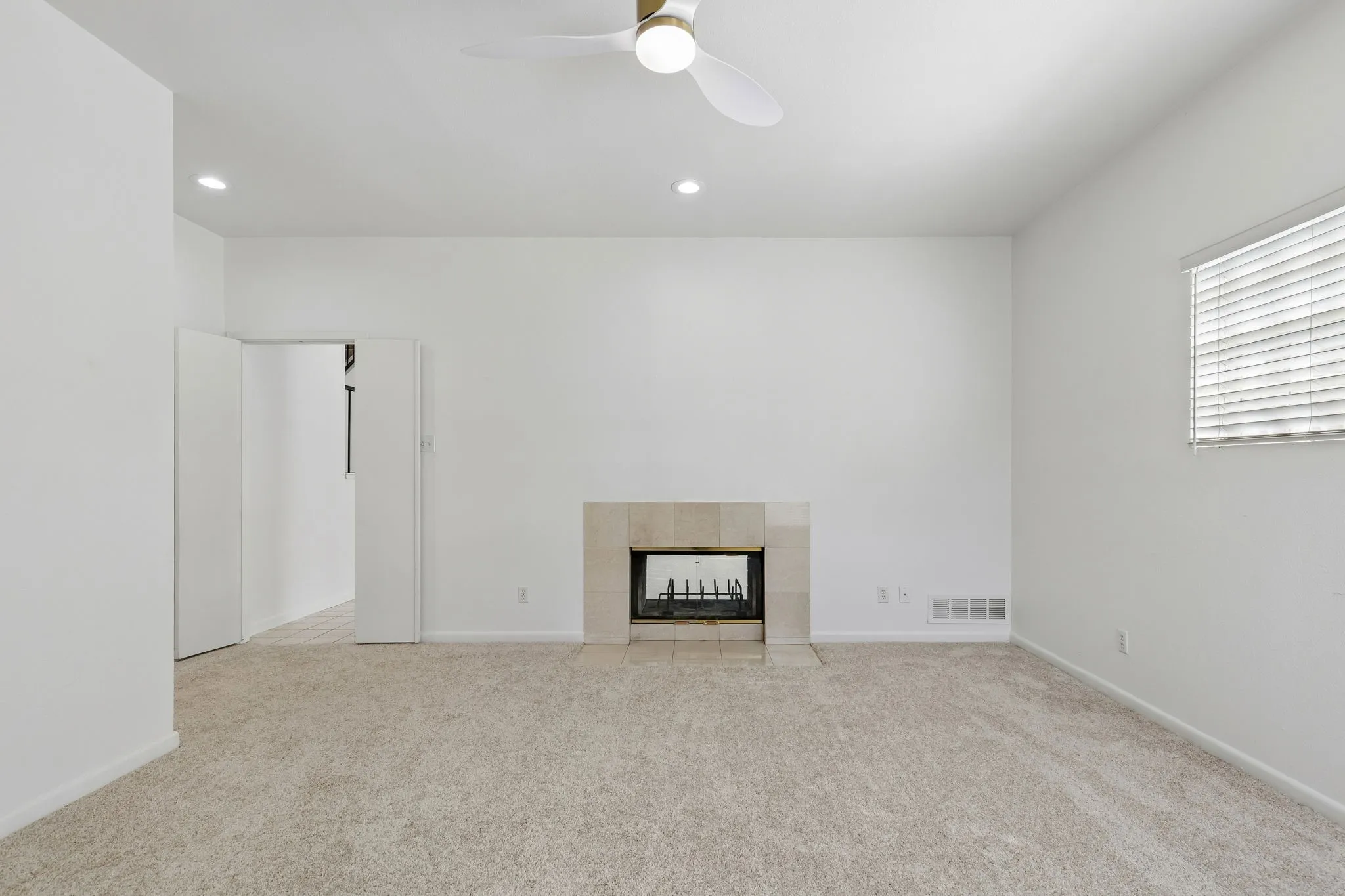 Unfurnished primary bedroom with ceiling fan, light carpet, recessed lighting, and fireplace