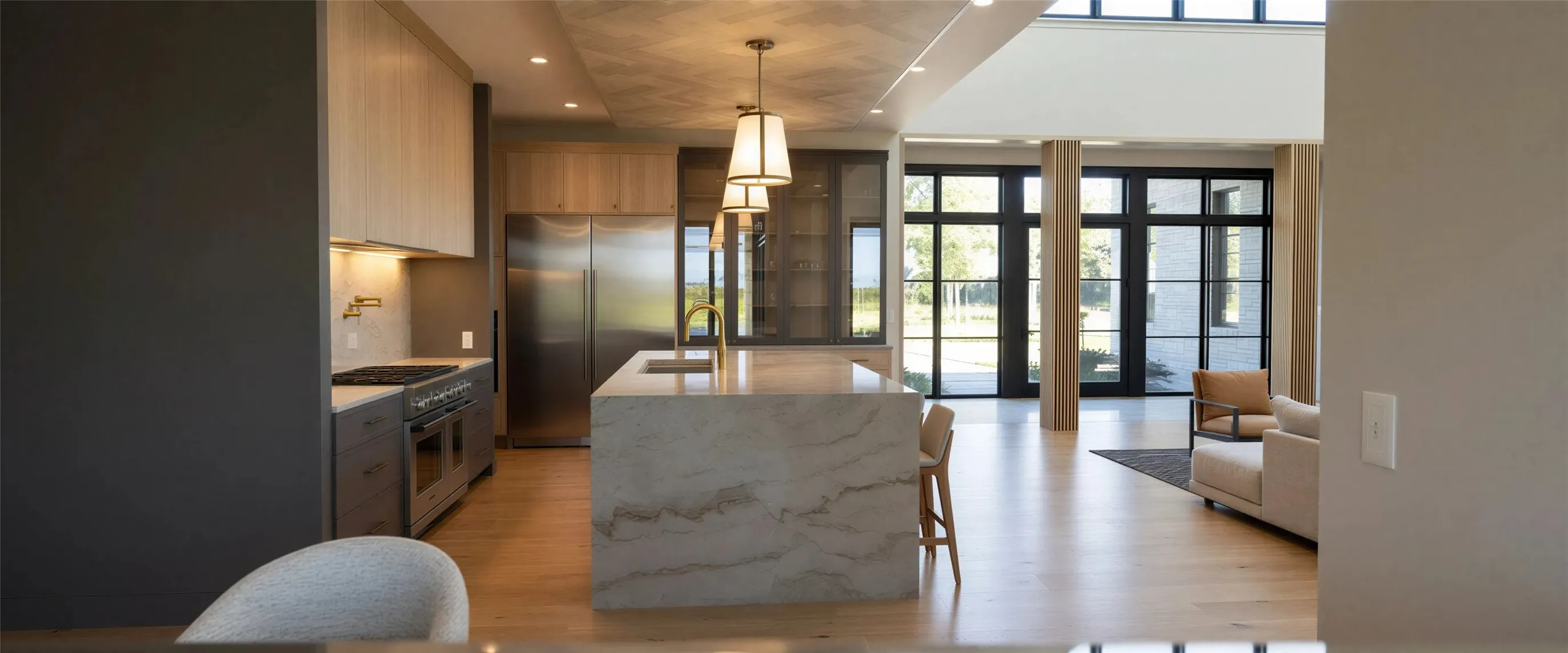 Kitchen with premium appliances, light stone counters, pendant lighting, an island with sink, and light wood-style floors
