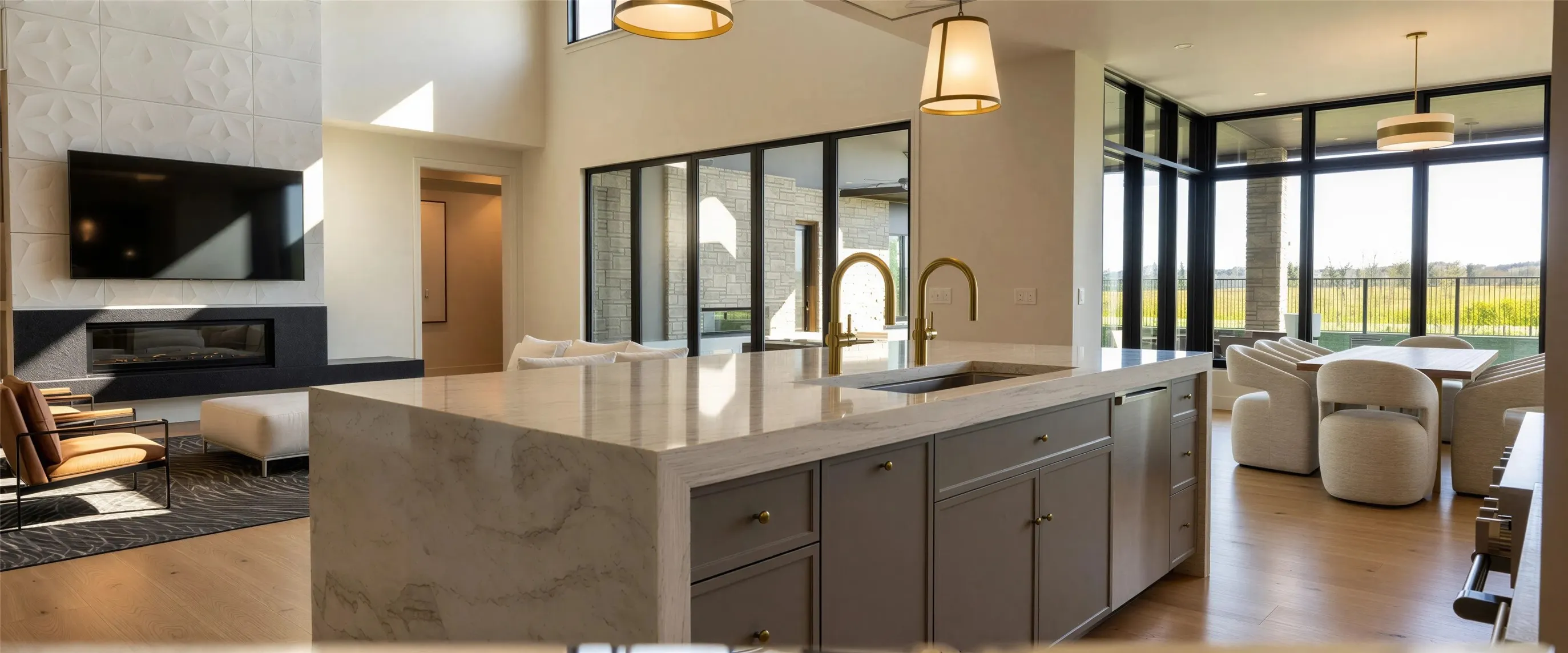 Kitchen featuring open floor plan, gray cabinets, light stone counters, an island with sink, and a glass covered fireplace