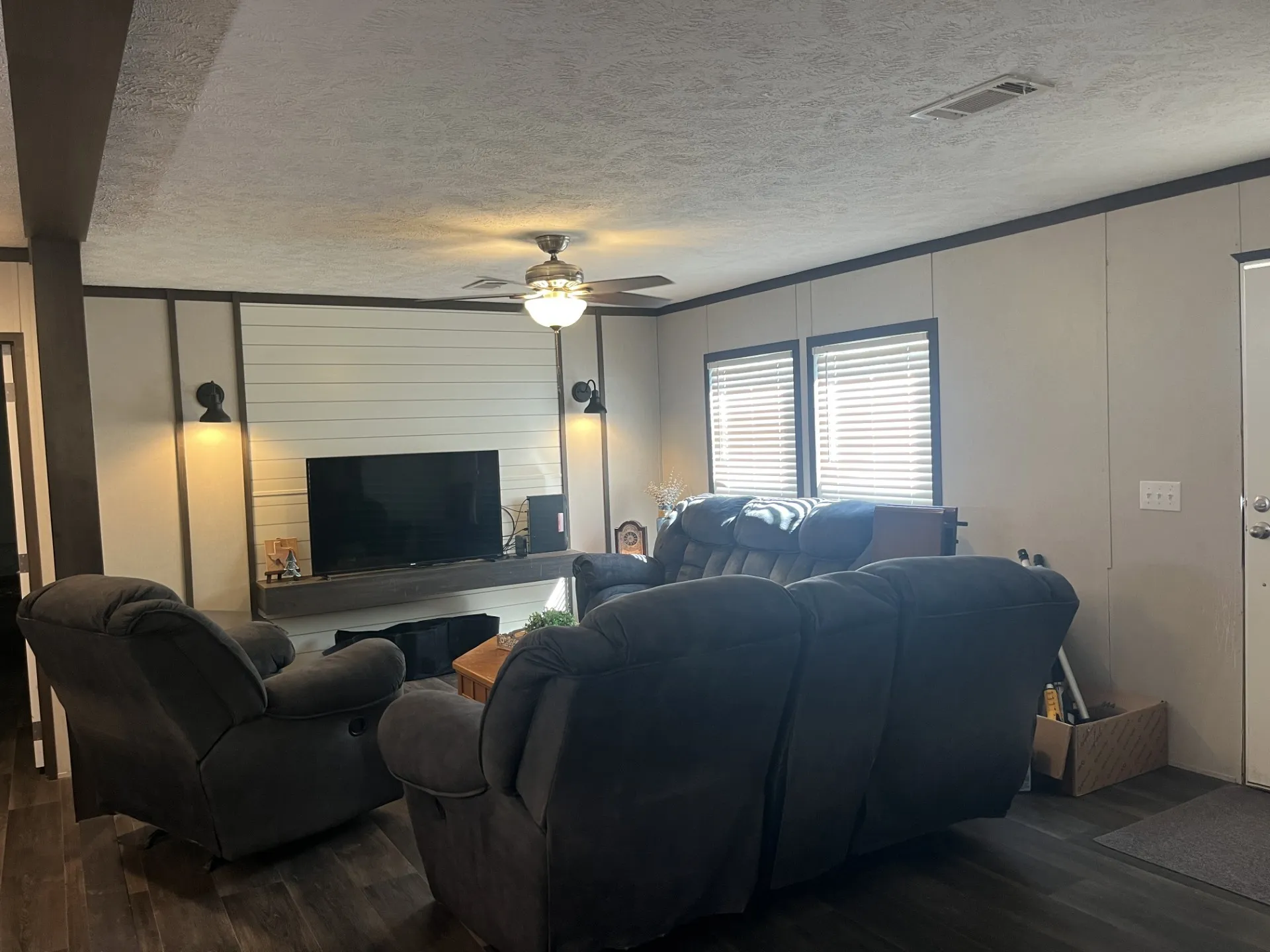 Living area featuring dark wood-style flooring, a textured ceiling, a ceiling fan, and a decorative wall