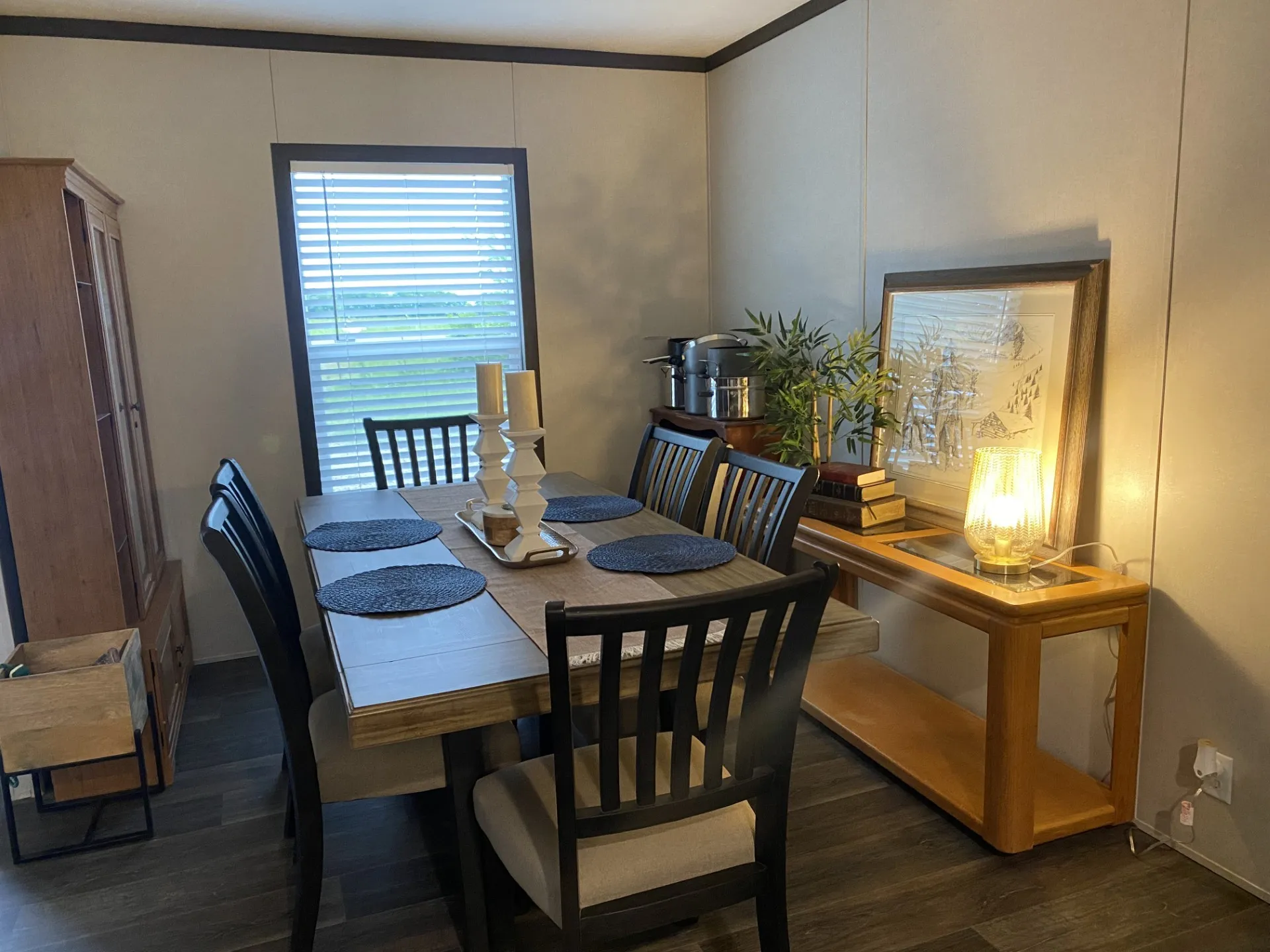 Dining area featuring wood-finish flooring, a window with horizontal blinds, and paneled walls with dark trim