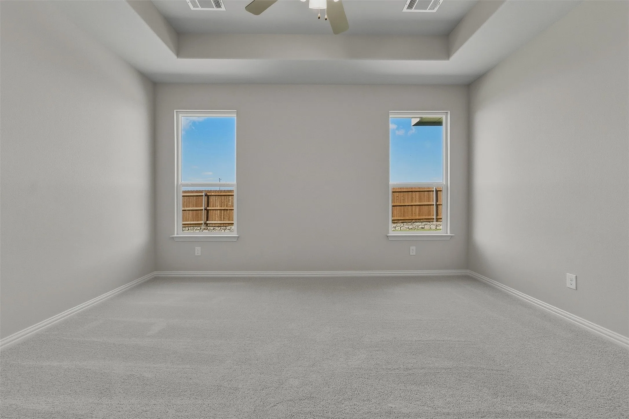 Tray ceiling with a ceiling fan, two windows, and light gray carpeting