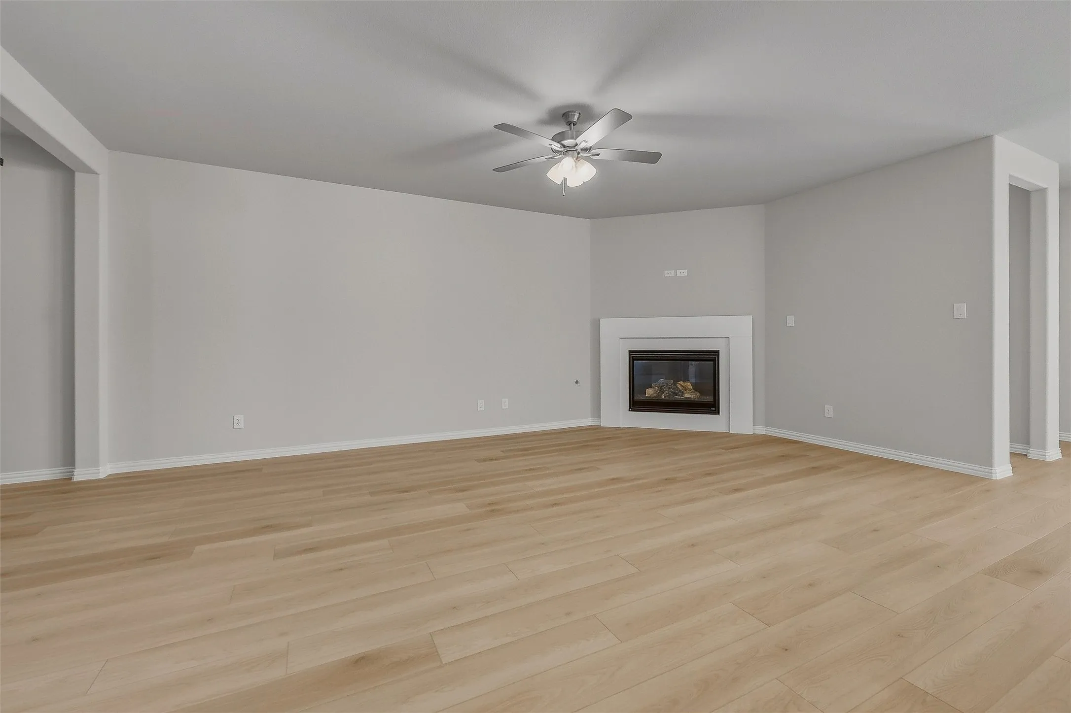 Spacious room with wood-finish flooring, a built-in fireplace with a white mantel, and a ceiling fan with integrated lighting