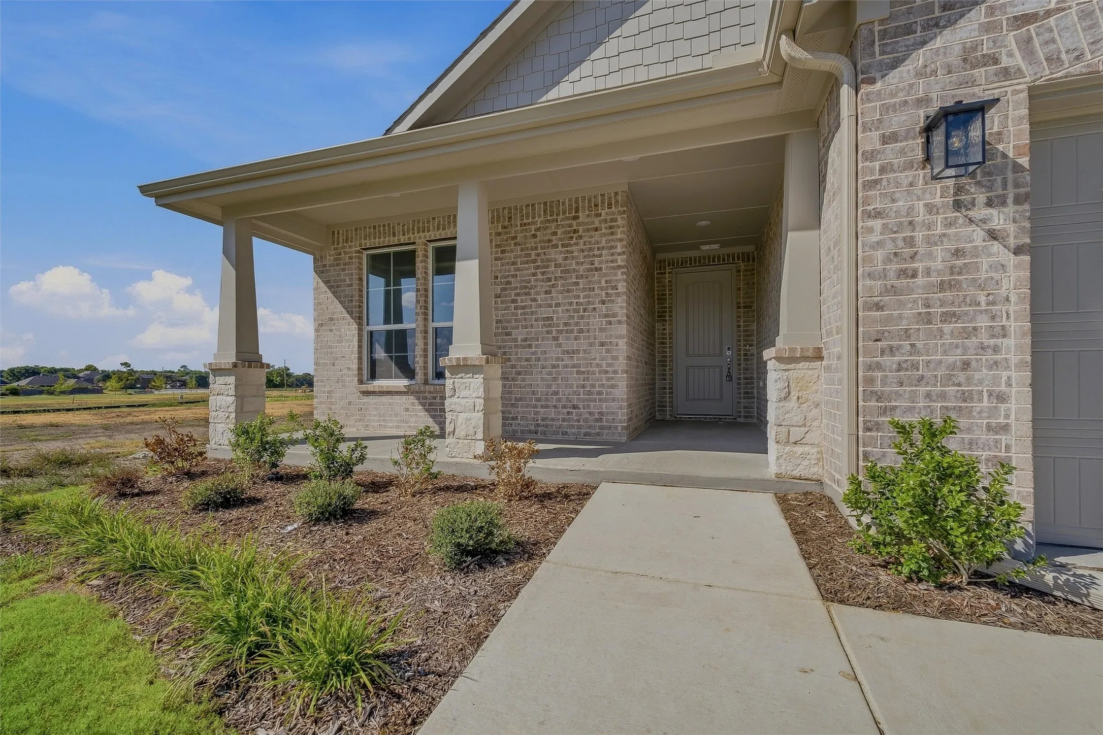 Covered entry featuring a light brick facade with stone accents, an exterior lantern fixture, and a paneled front door